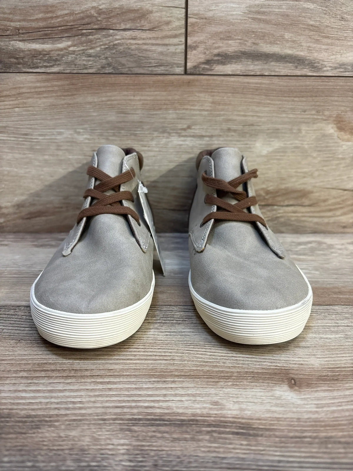 Kids' gray casual sneakers with white soles and brown laces on wooden floor