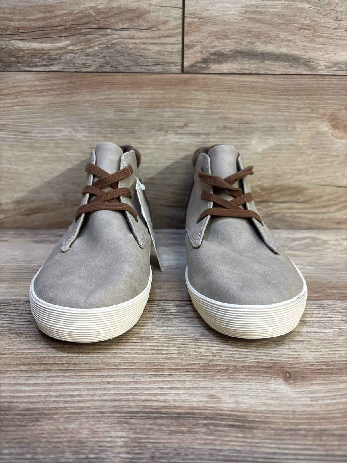 Kids' gray casual sneakers with white soles and brown laces on wooden floor