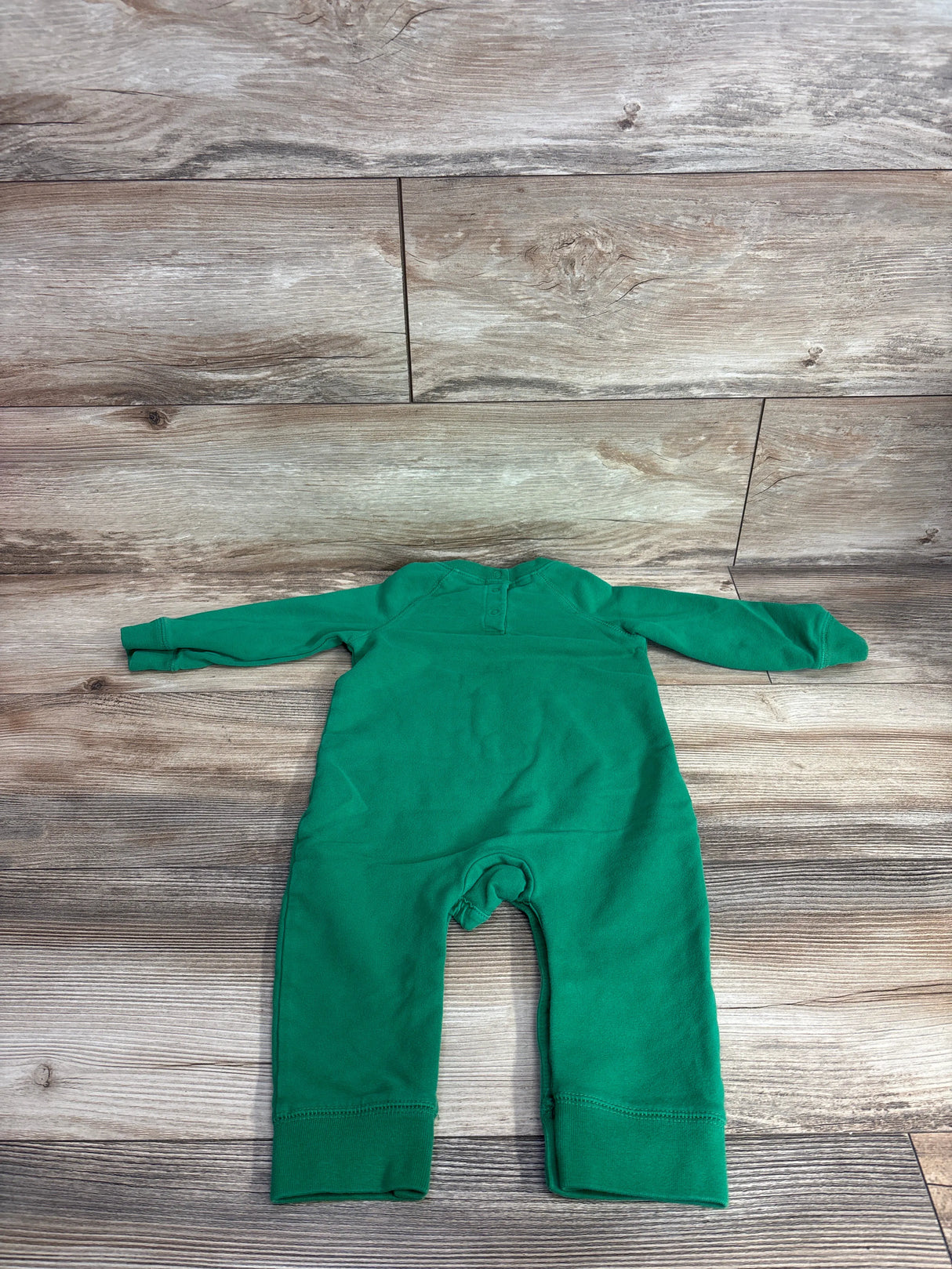 Green long sleeve baby romper laying flat on wooden surface