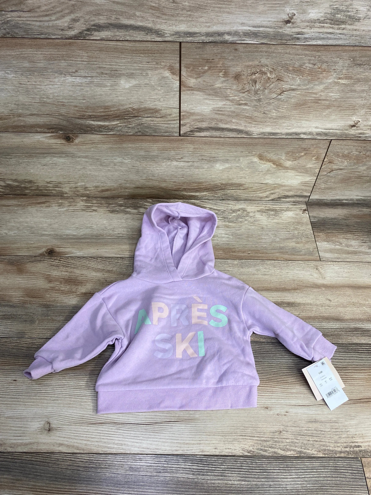 Light purple toddler hoodie with 'APRES SKI' text, laid flat on wood floor, resale kids clothing