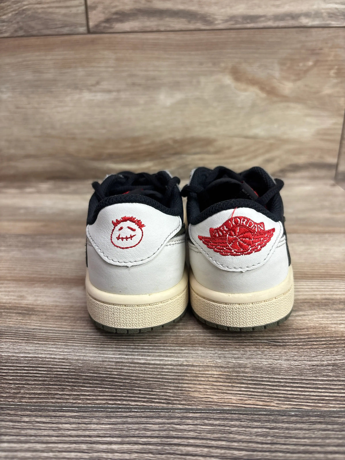 Rear view of Travis Scott x Air Jordan 1 Retro Low OG SP PS Olive sneakers showcasing red heel logos with wood floor background