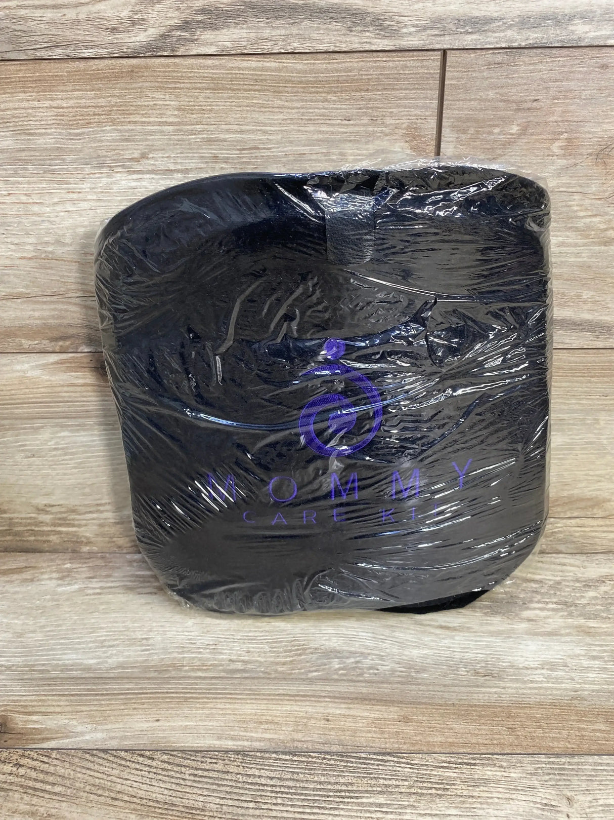 Front view of black Mommy Care Kit lower back support belt in plastic wrap with purple logo on wood background