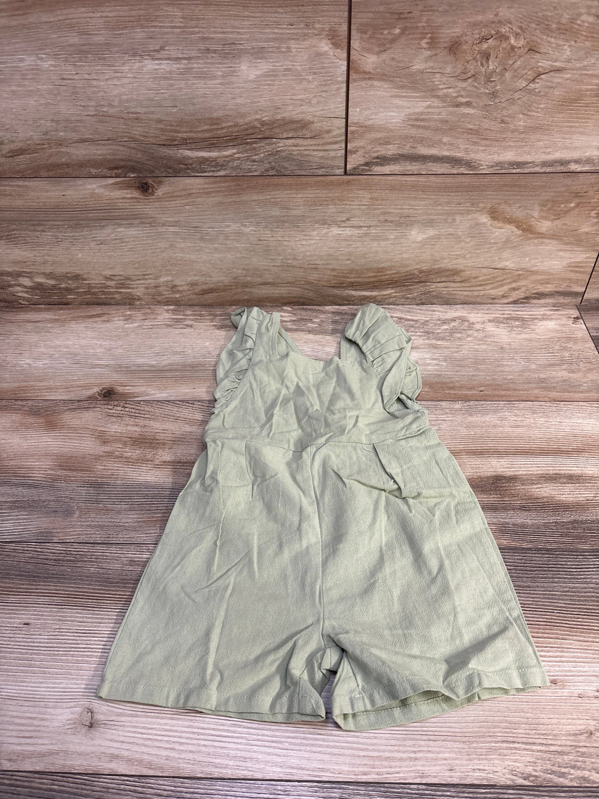 Flat lay of green Shein flutter-sleeve shortie romper size 18-24 months showcasing ruffled sleeves and gathered waist on wood plank background