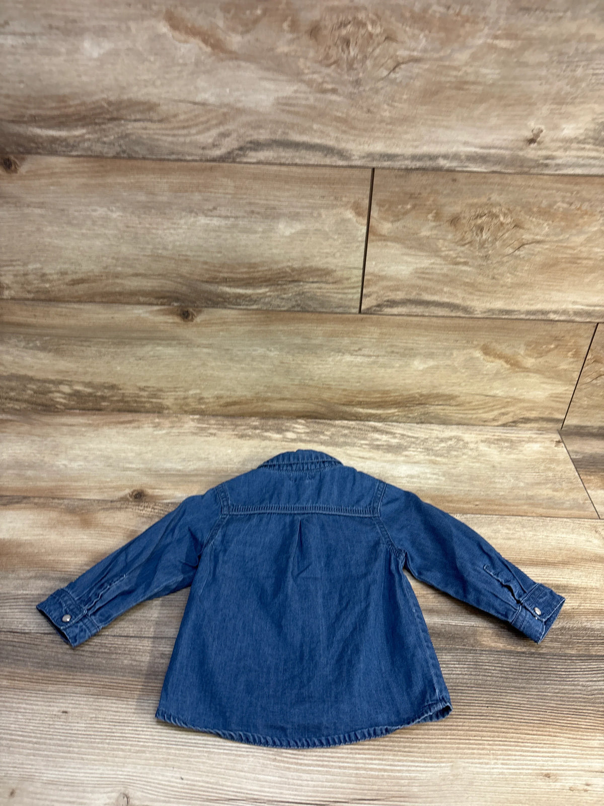 Back view of baby chambray long-sleeve button-up shirt showcasing back yoke pleat and buttoned cuffs on wood floor background