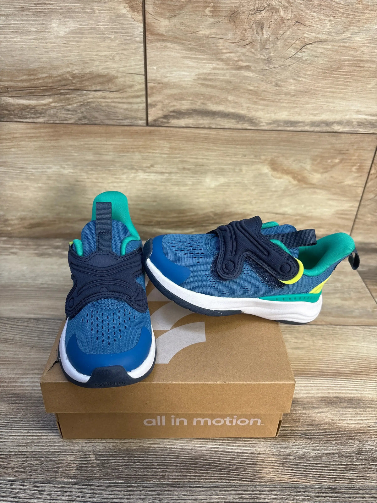 Blue and teal kids athletic sneakers with hook-and-loop straps on a shoe box with wood background