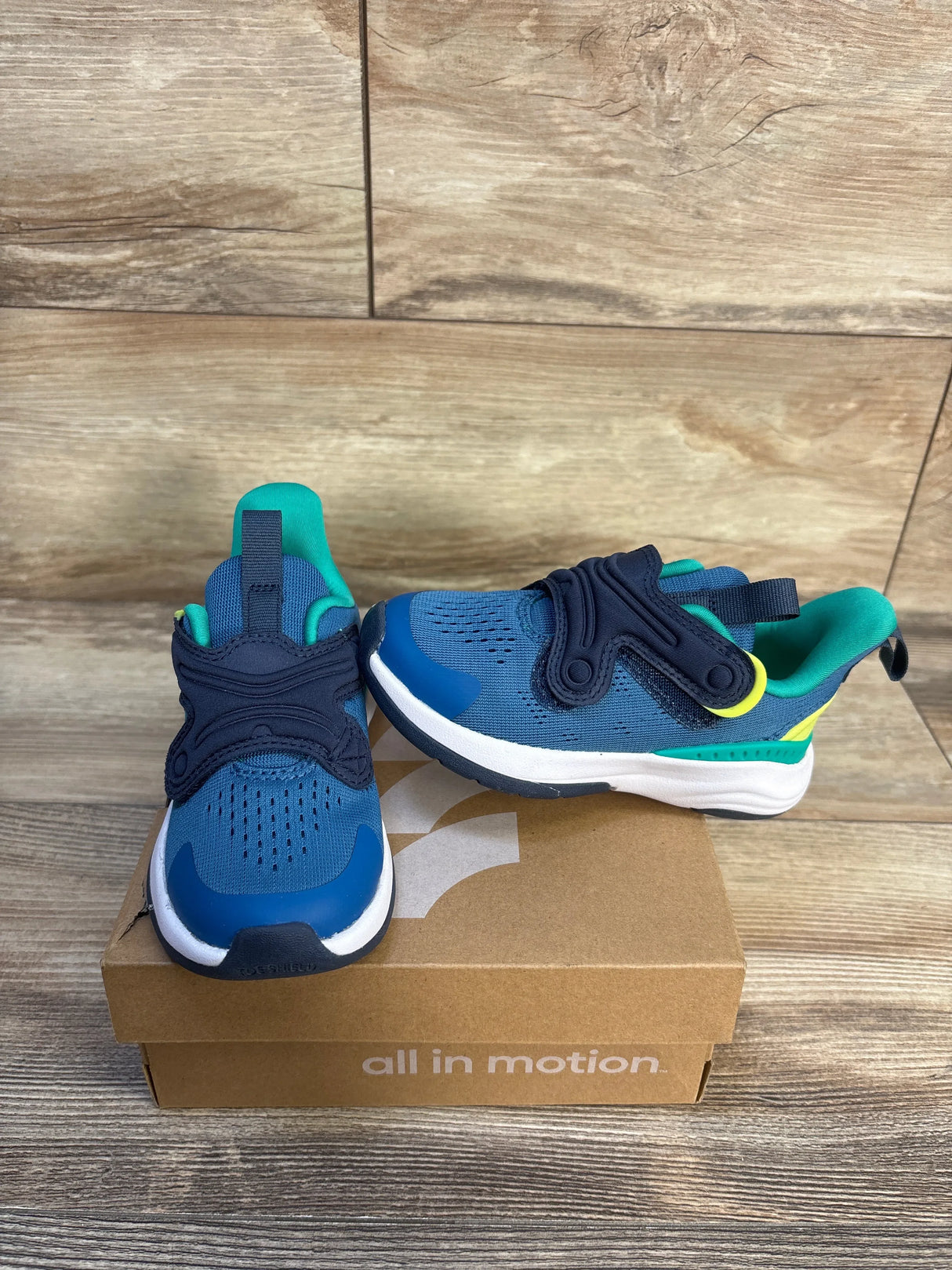 Blue and teal kids athletic sneakers with hook-and-loop straps on a shoe box with wood background