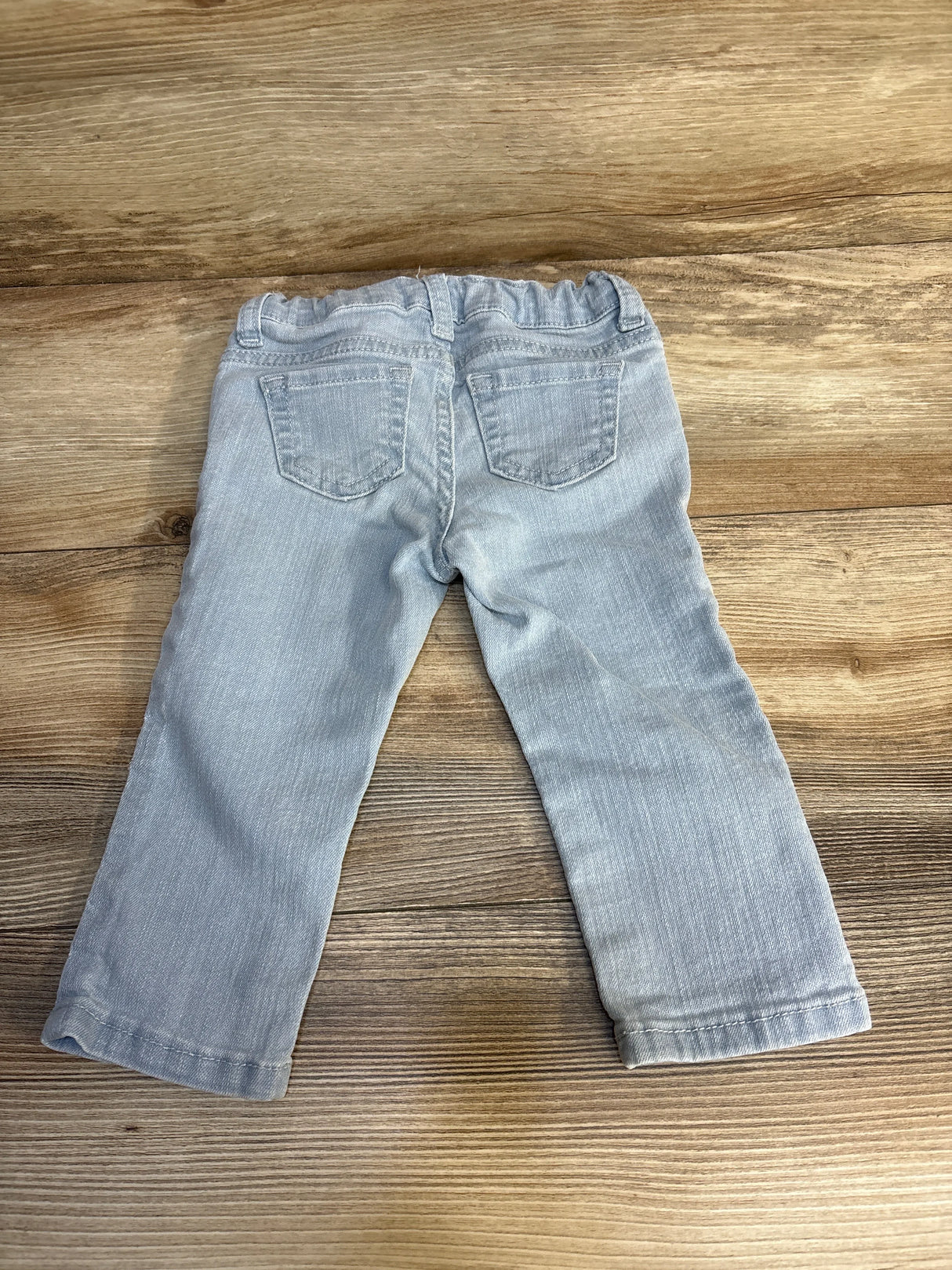 Light blue toddler jeans with elastic waist, laid flat on wood floor — kids clothing resale