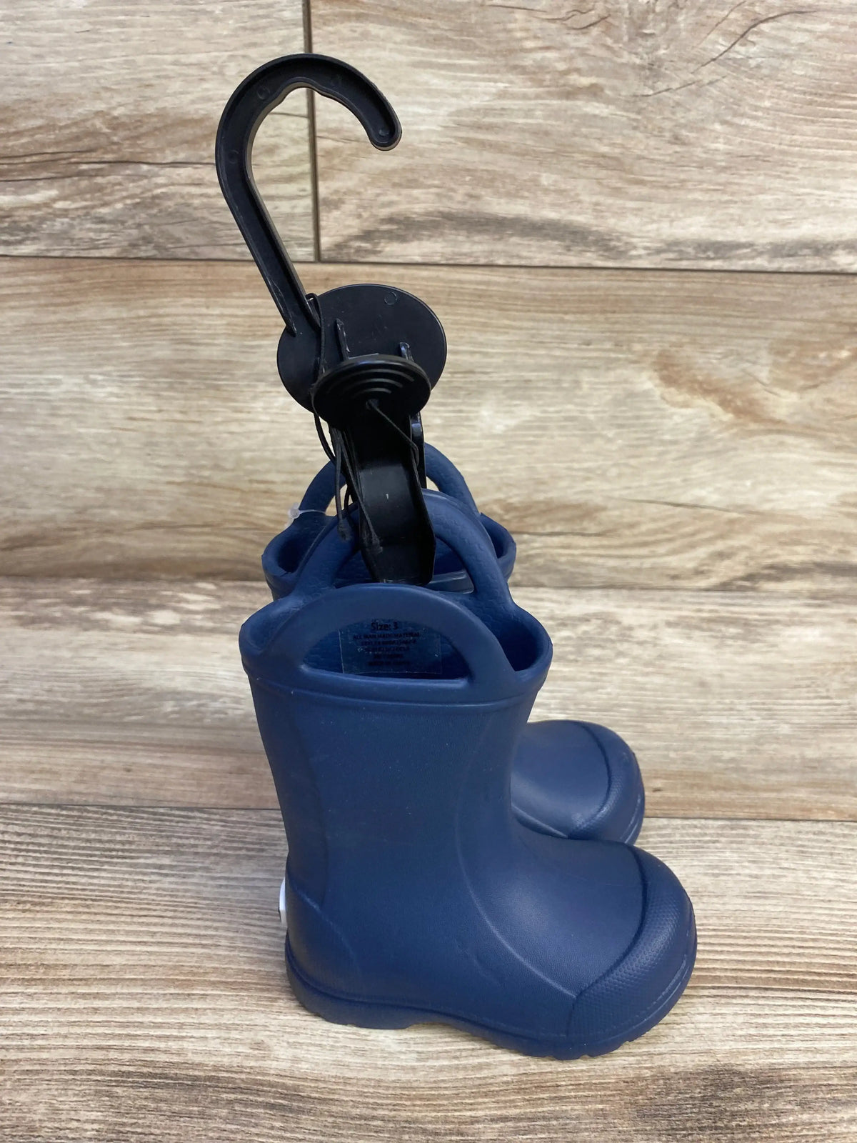 Rear three-quarter view of BEARPAW EVA navy toddler rain boots showcasing easy pull-on handles with light wood background