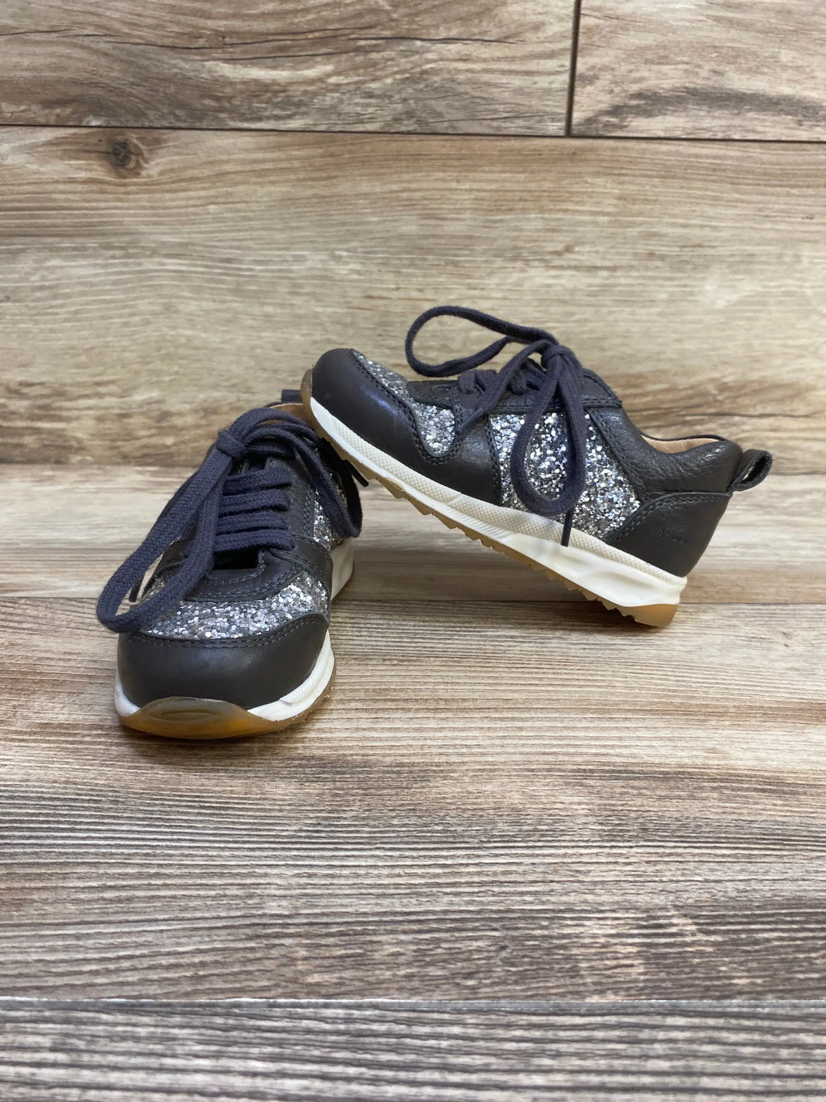 Three-quarter view of Angulus toddler glitter sneakers in grey showing glitter panels and laces with wood floor background