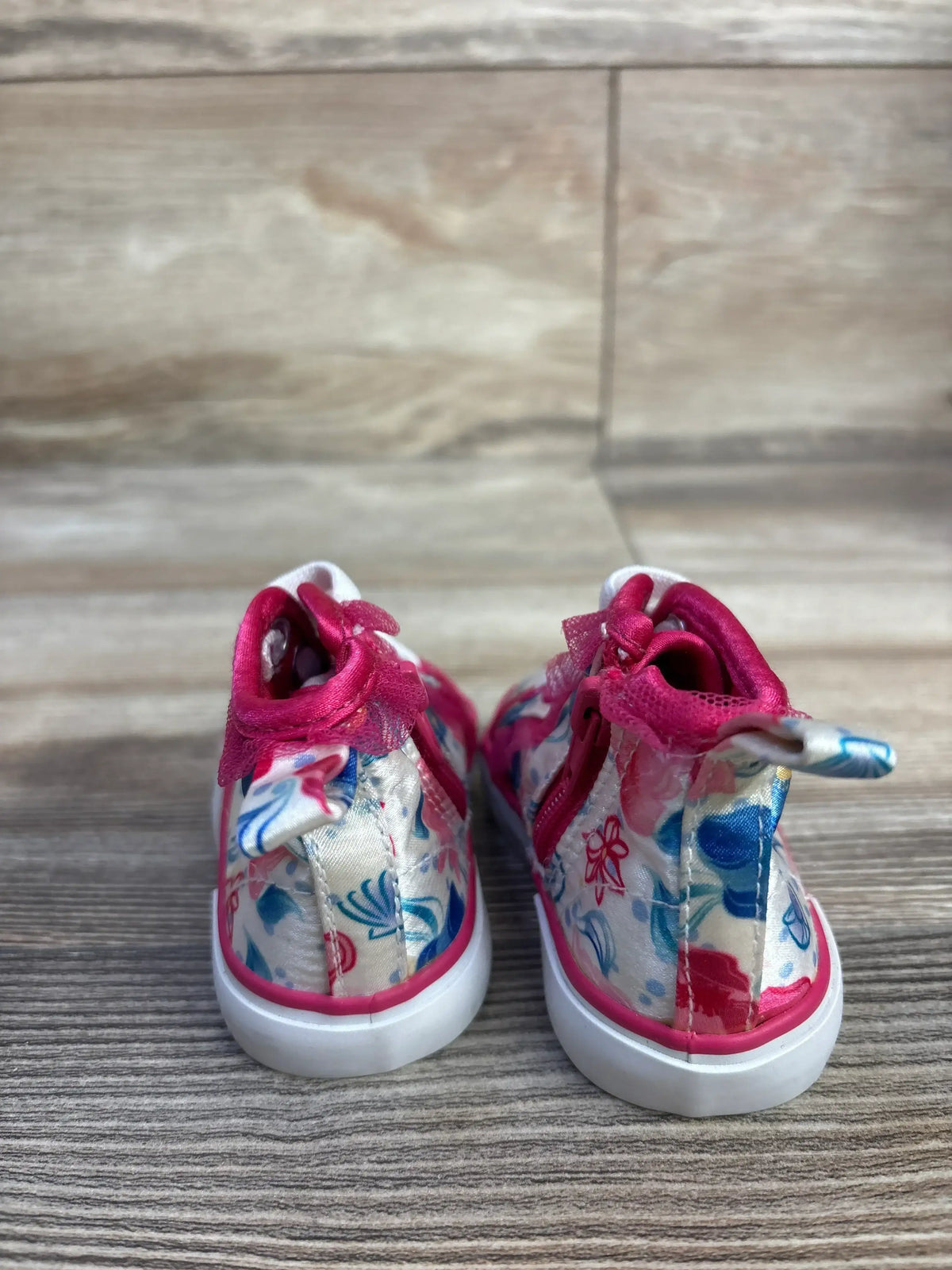 Rear view of toddler Disney floral high-top sneakers in pink showing satin floral print, back zipper pull and bow on wood floor
