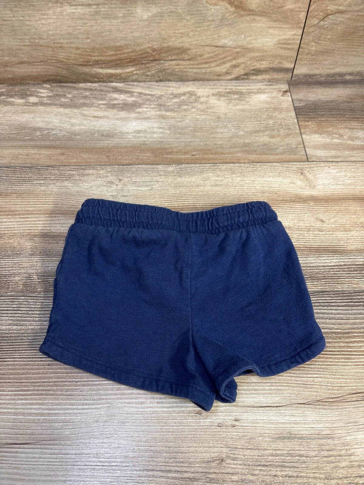 Flat-lay front of Jumping Beans navy toddler shorts showcasing elastic waistband and cotton texture on wood surface
