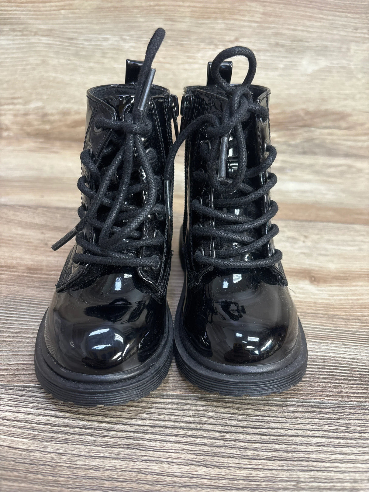 Black patent leather lace-up toddler boots on a wood background