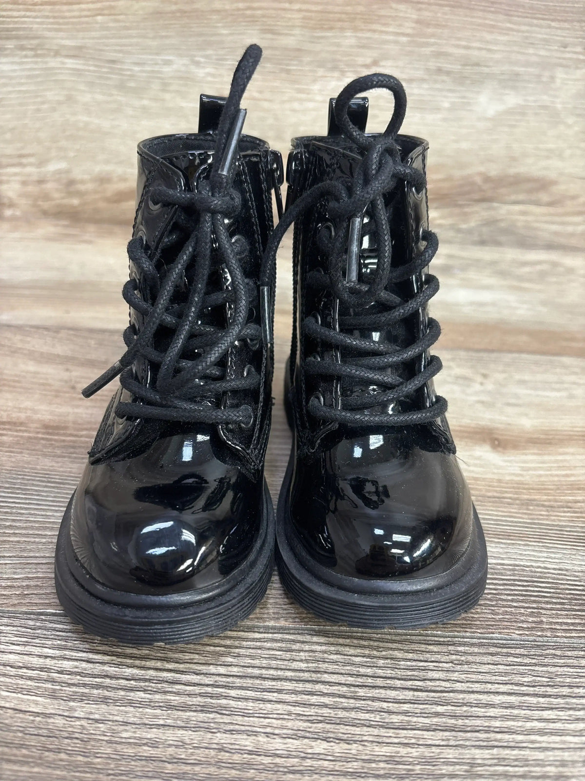 Black patent leather lace-up toddler boots on a wood background