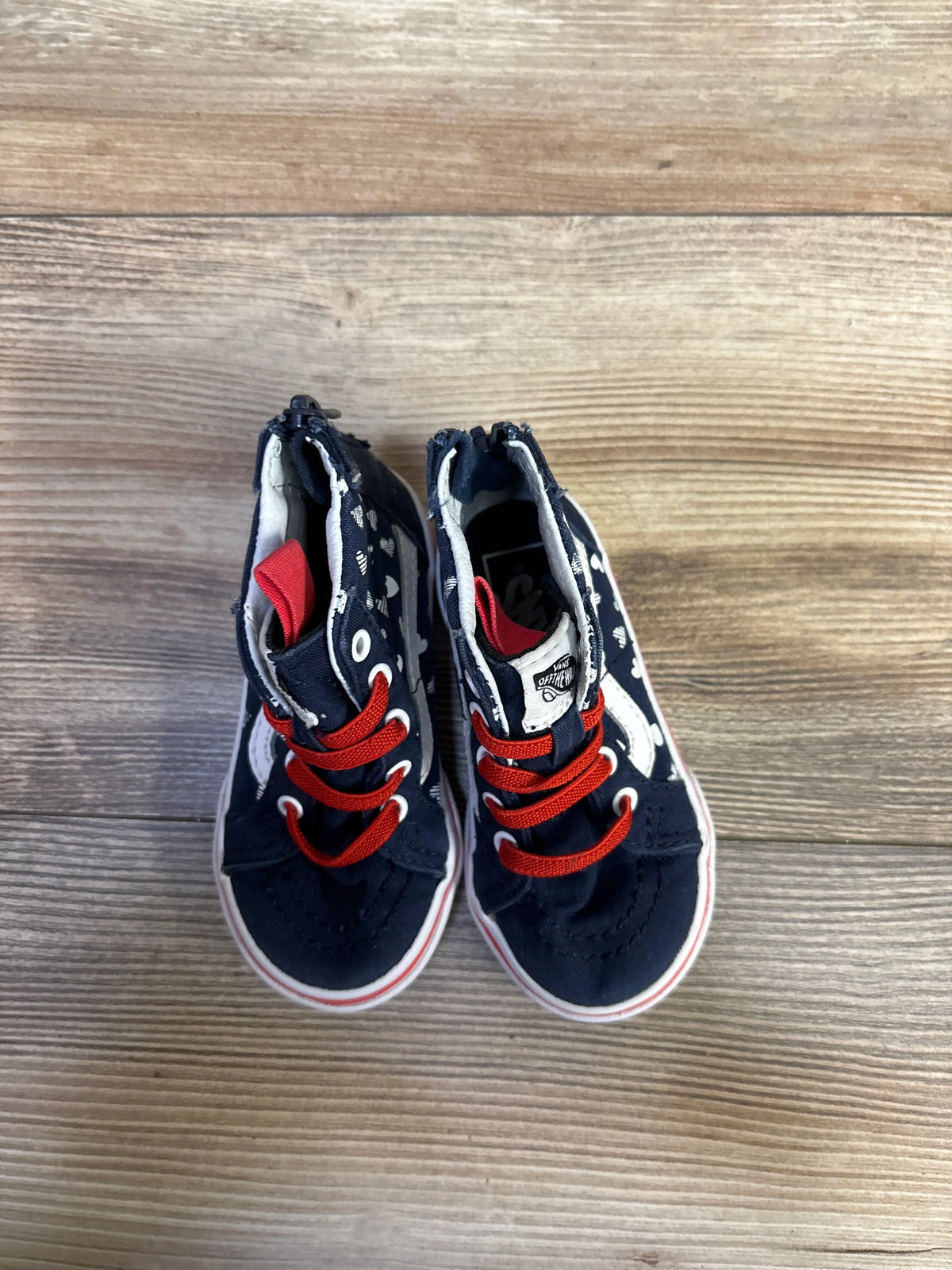 Top view of navy Vans Sk8-Hi Zip sneakers with red laces, white heart print and white rubber sole on wood floor