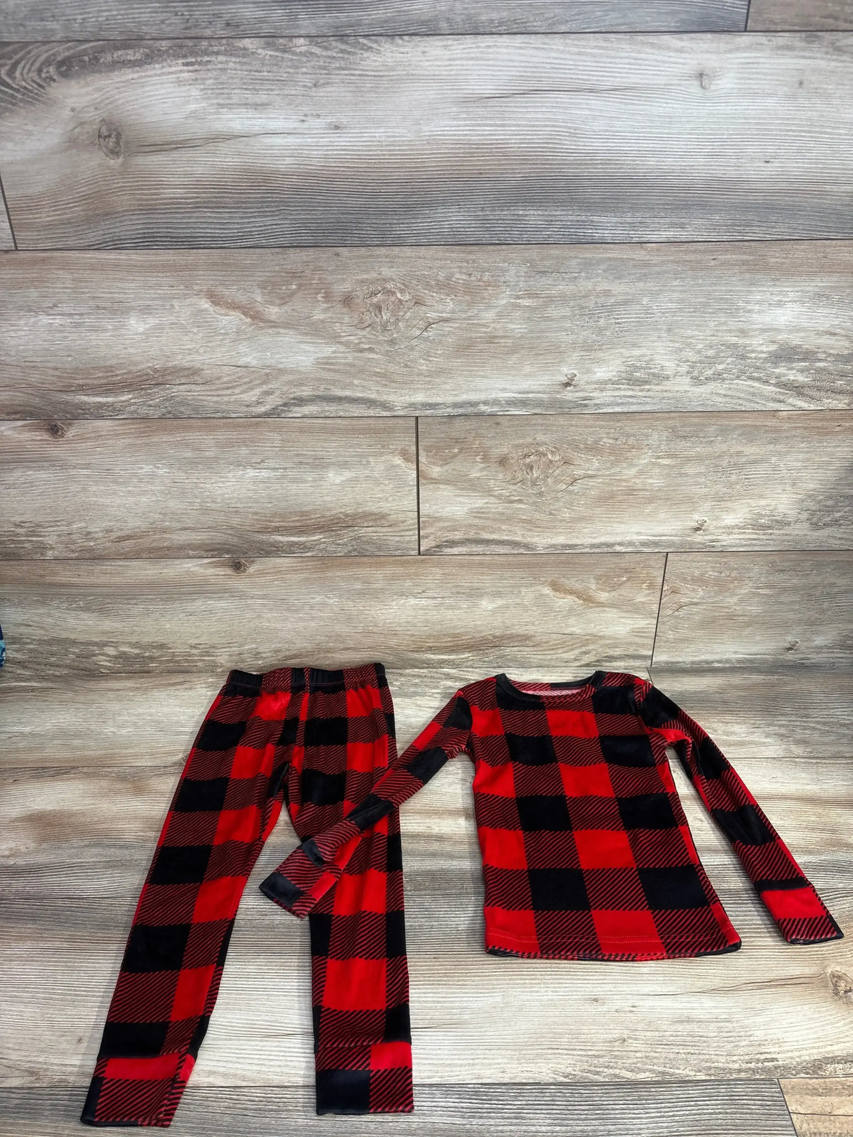 Red and black plaid kids pajama set with long sleeves and pants on wood floor