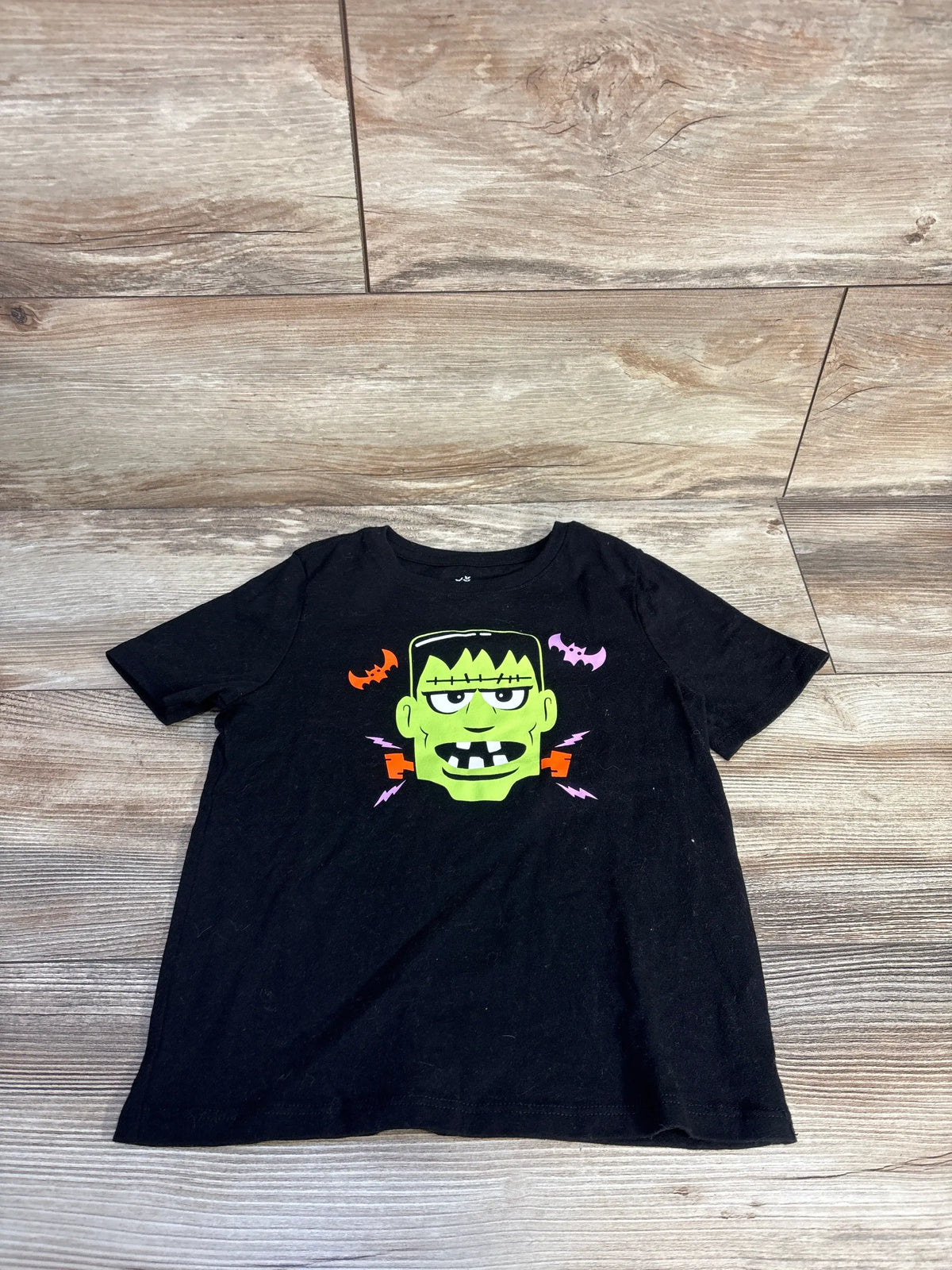 Front view of black toddler Halloween Frankenstein shirt showcasing colorful Frankenstein graphic with bats on a wood floor