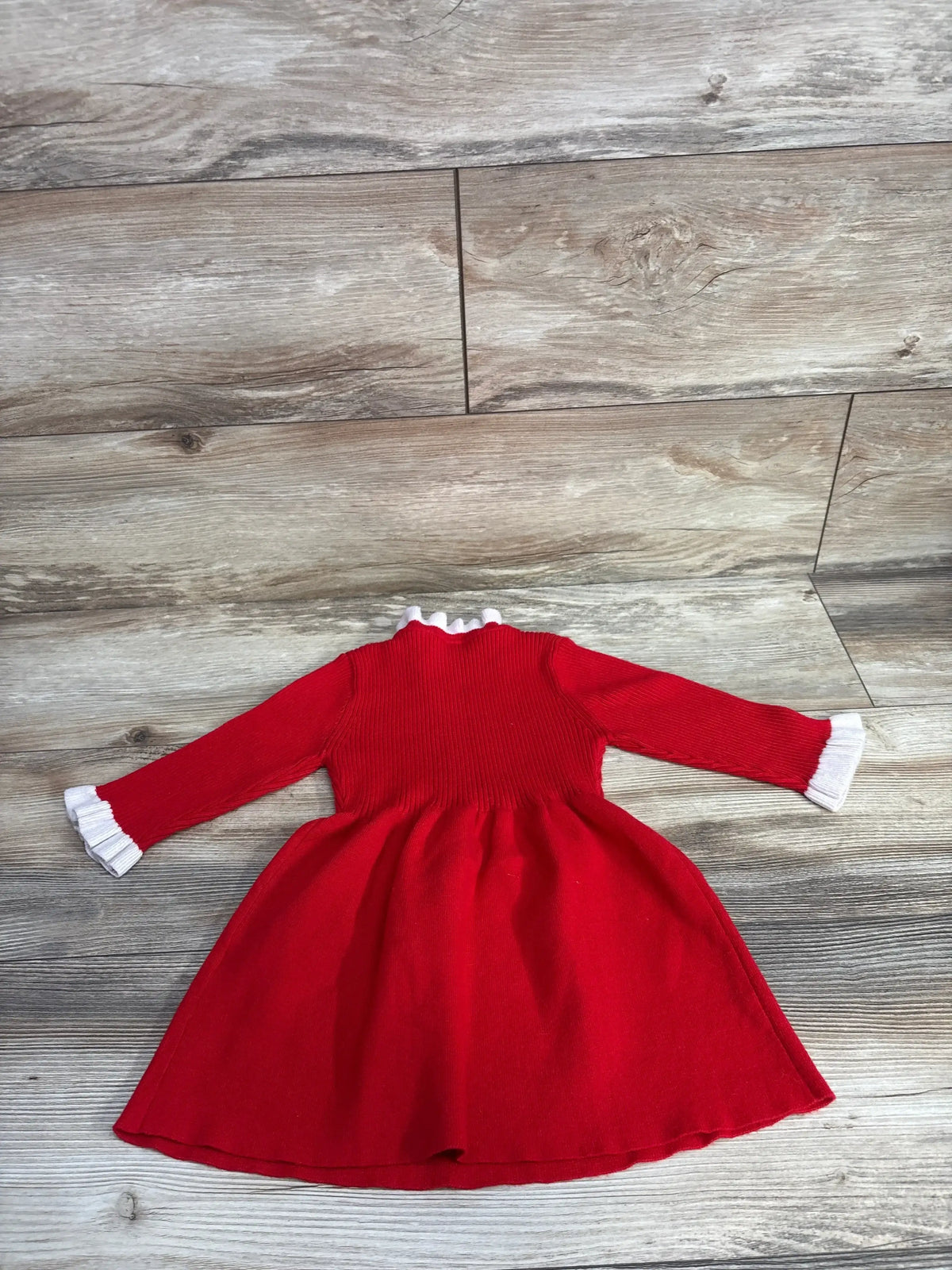 Red baby dress with white trim, long sleeves, smocked bodice on wood floor — kids clothing