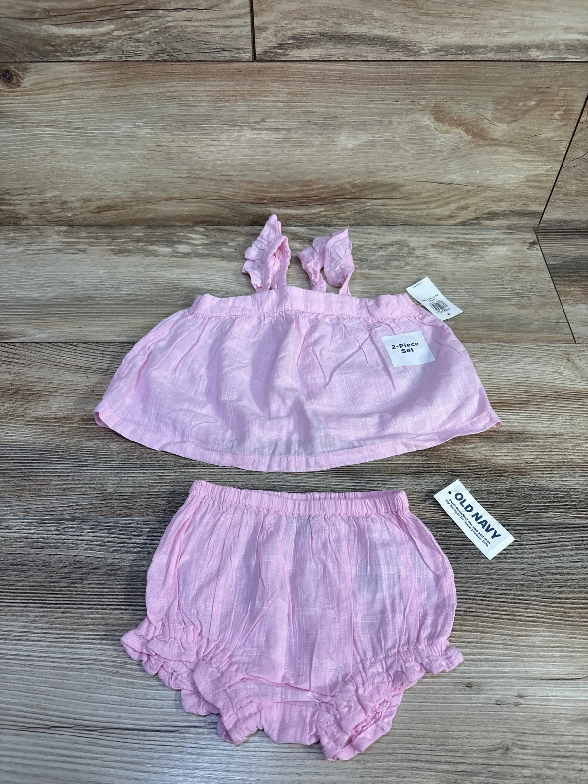 Flat lay of pink Old Navy 2-piece tank and shorts (3-6 months) showing ruffled straps and elastic waist on wood background