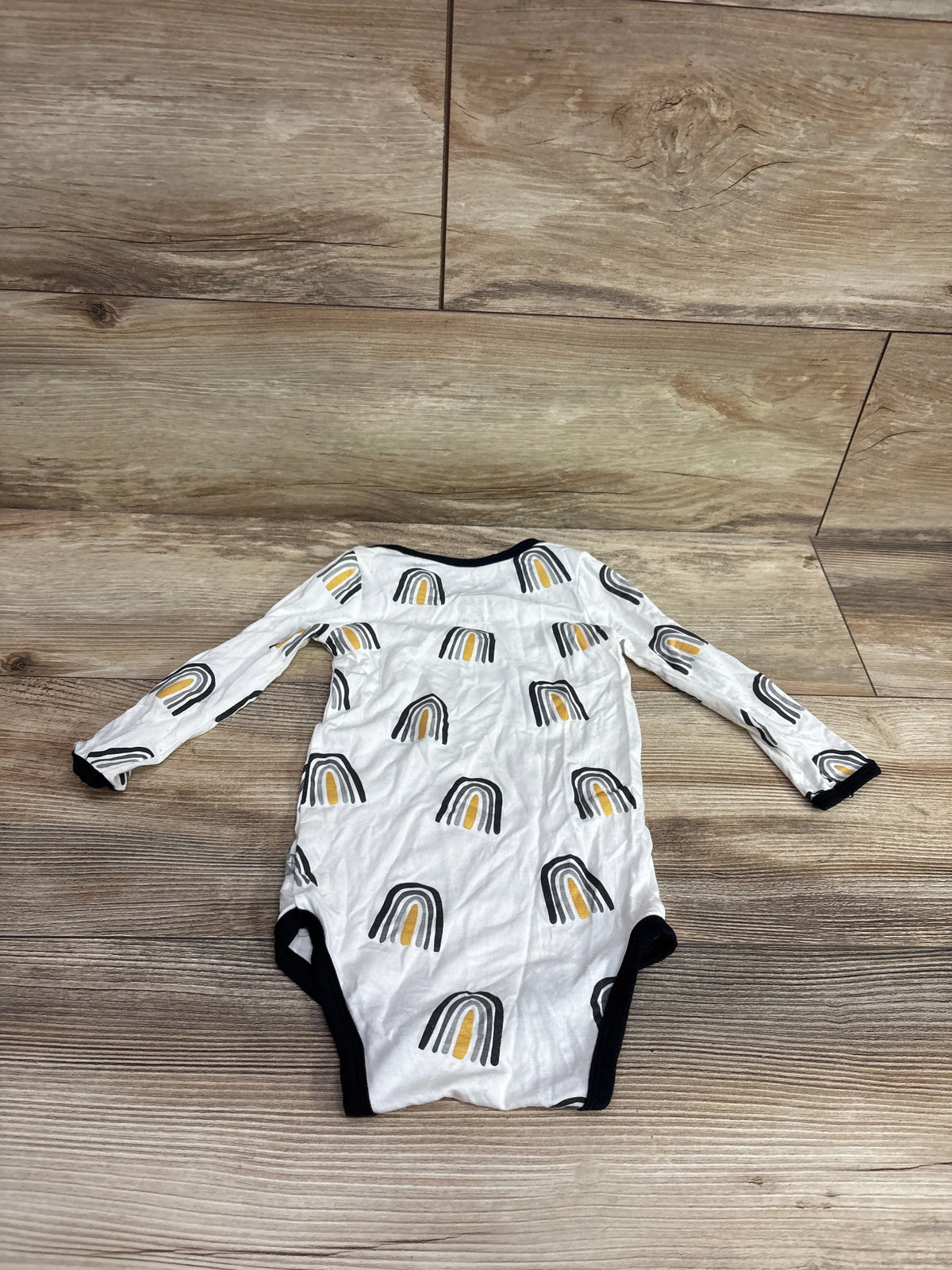 Front view of white Kyte Baby bamboo long sleeve bodysuit, size 18 to 24 months, with rainbow print and black trim on wood floor