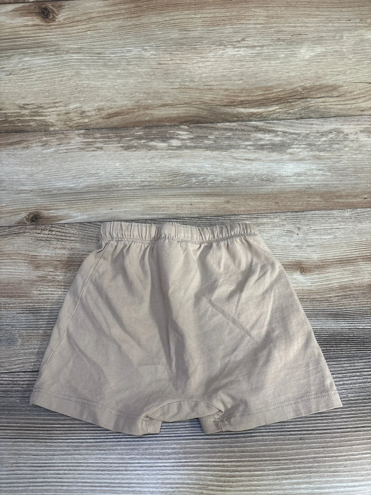 Flat lay of beige H&M baby pull-on shorts showing elastic waistband and hem on wood background