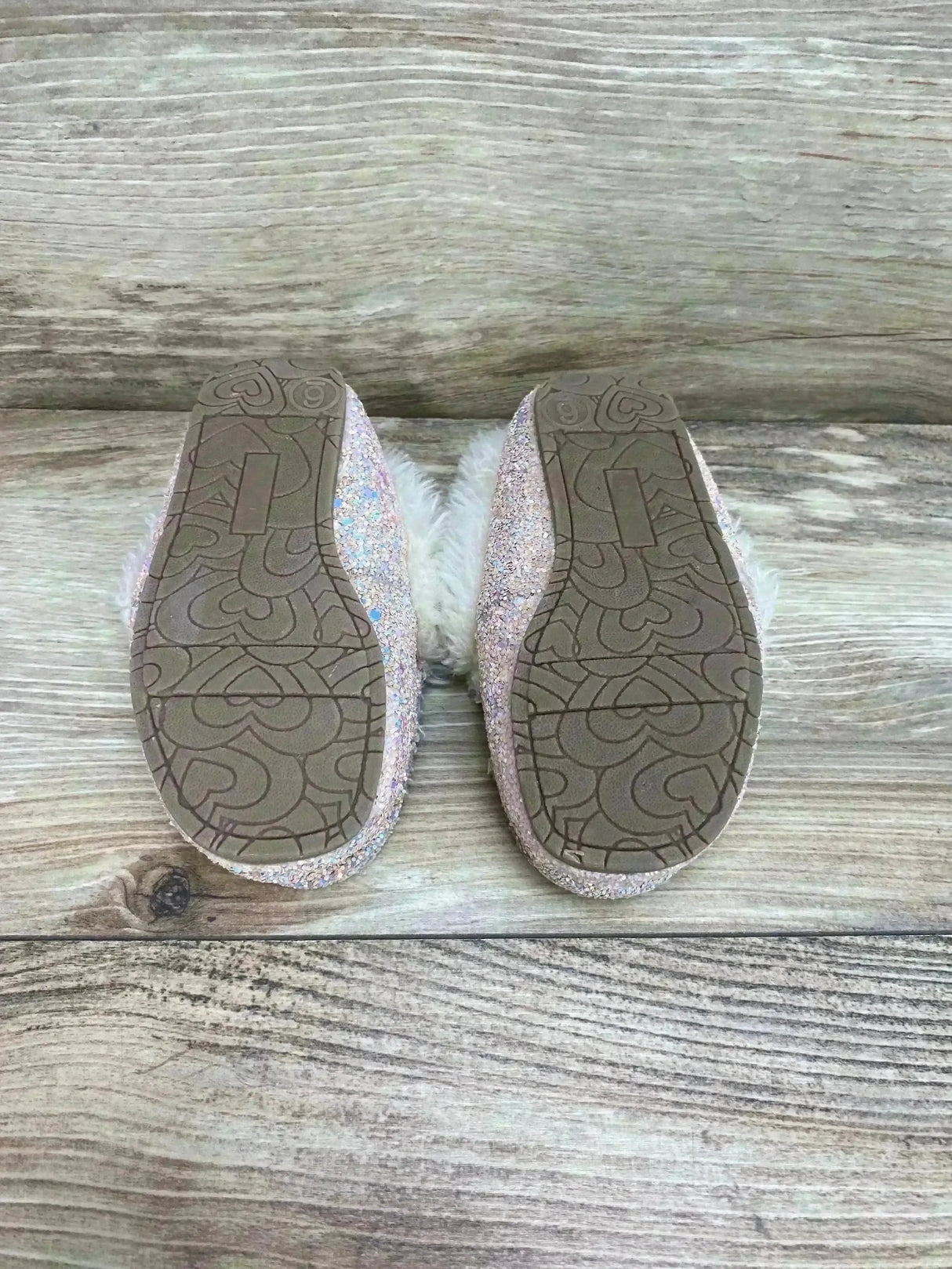 Bottom view of Cat & Jack Medora toddler slippers size 6C showing heart-patterned rubber soles and glittery pink exterior with white faux fur on wood