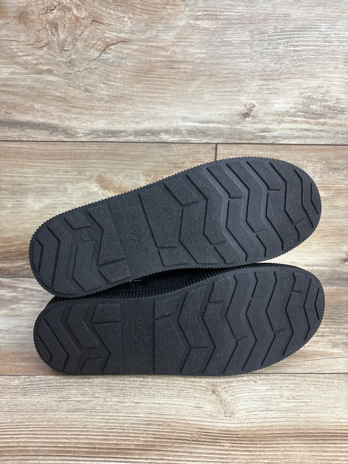 Bottom view of Cat and Jack Holland shearling-style kids boots size 5Y showing textured black rubber soles on wood floor