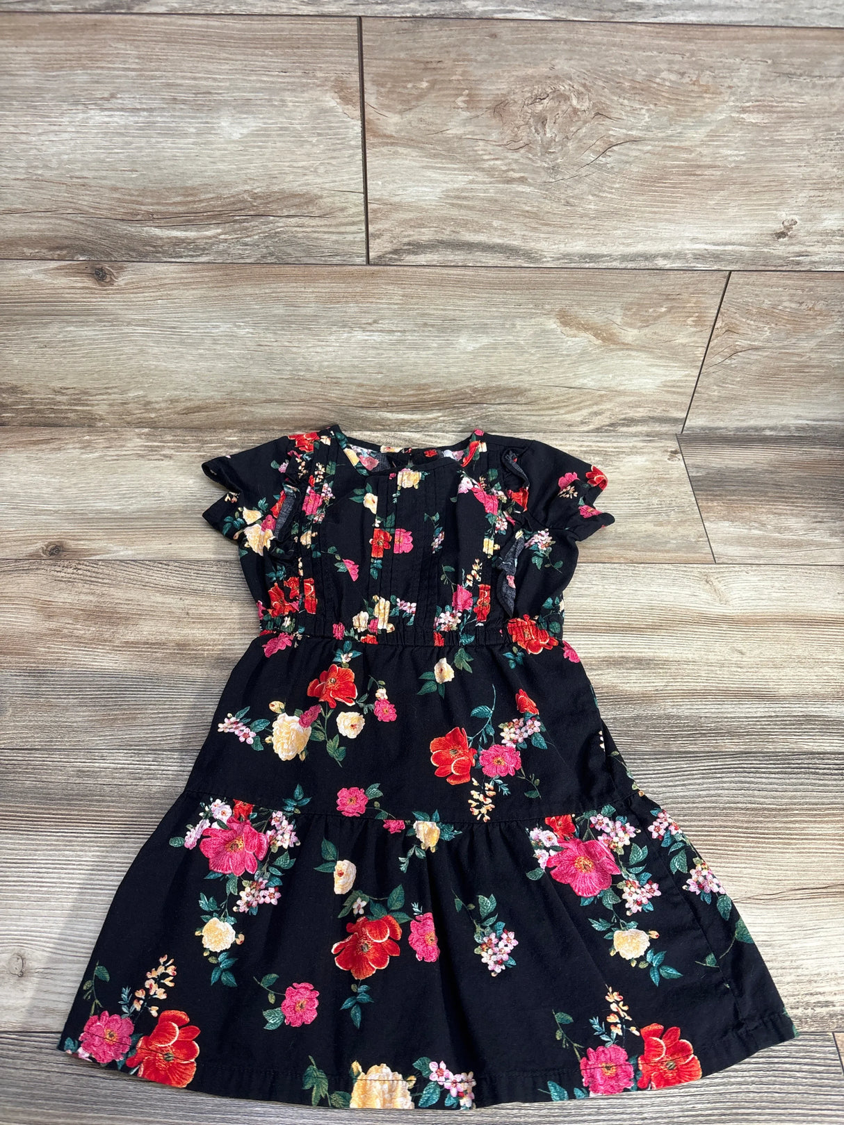 Girls black floral dress with colorful flower print, short sleeves, laid on wooden floor