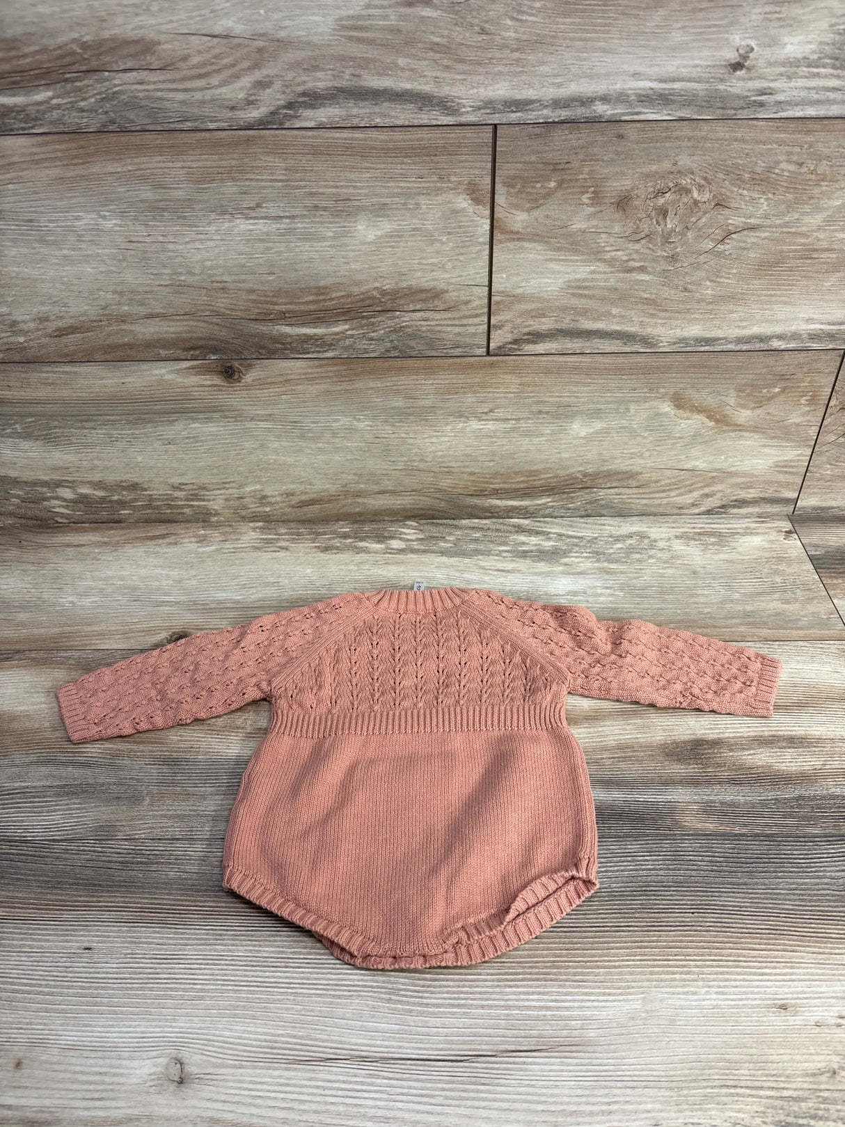 Pink knitted long sleeve baby romper with textured pattern on wooden floor, children's clothing