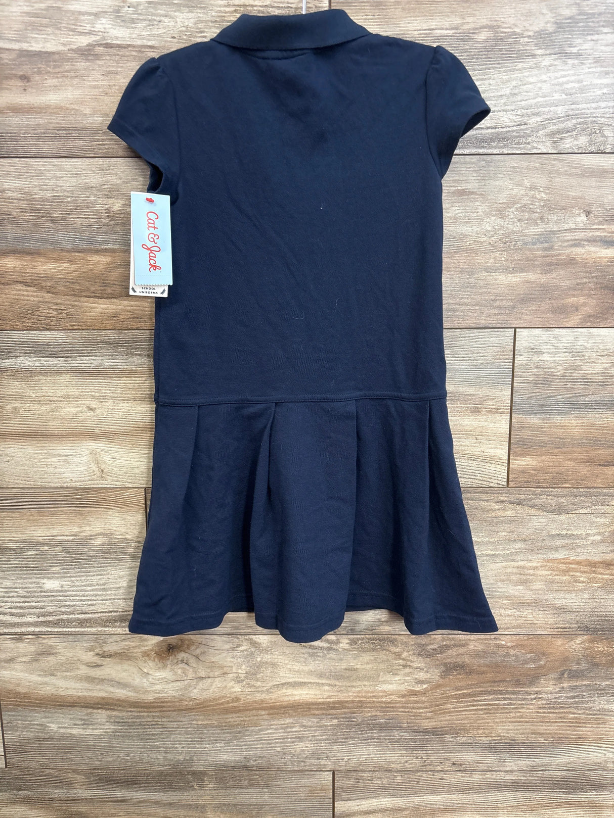 Back view of Cat and Jack navy pleated girls school uniform dress with polo collar and short sleeves, laid flat on wood floor