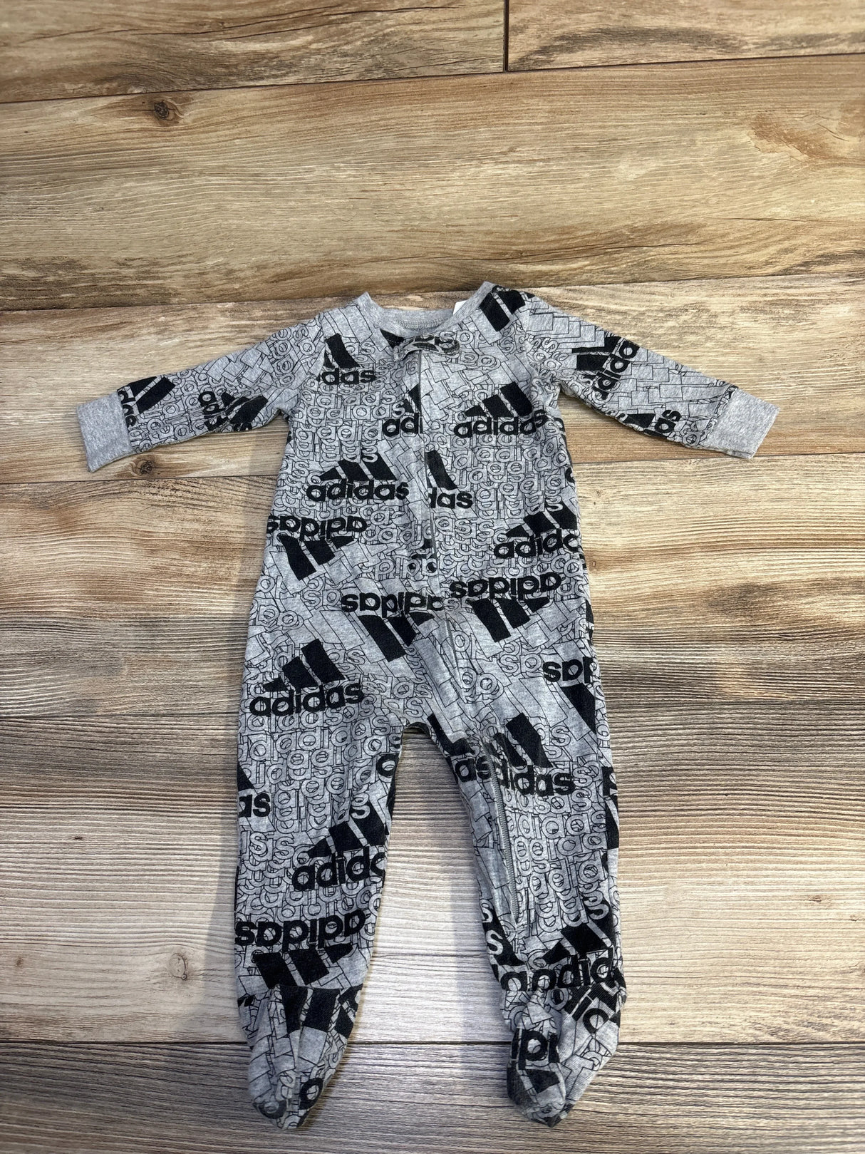 Gray Adidas baby onesie with black logo print laid flat on wooden floor, children's clothing