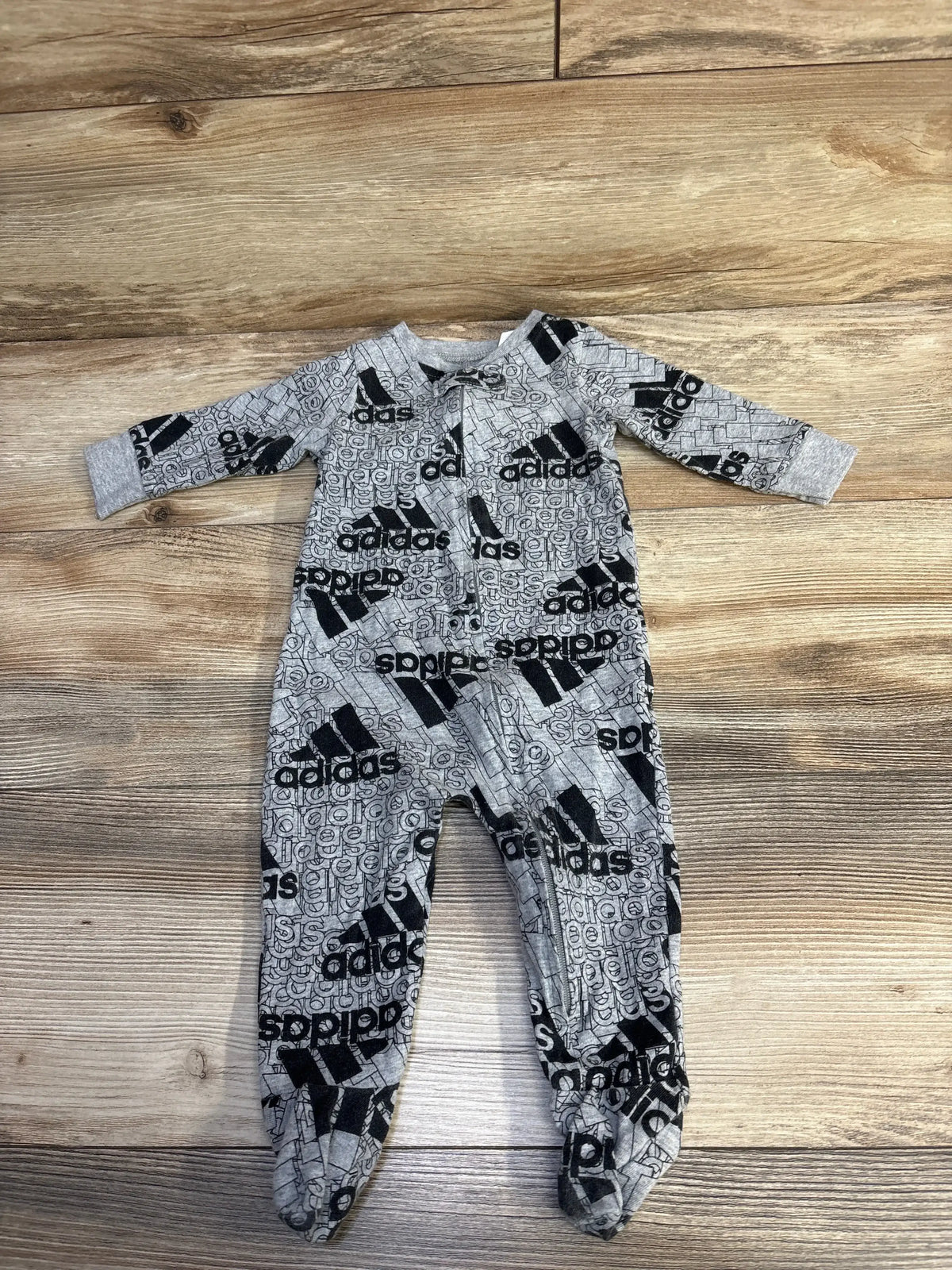 Gray Adidas baby onesie with black logo print laid flat on wooden floor, children's clothing