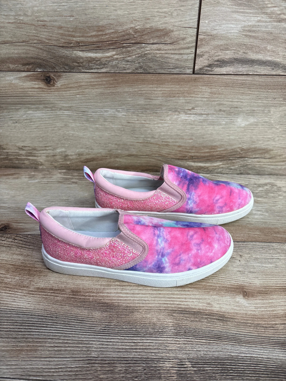 Pair of pink and purple tie-dye slip-on kids shoes with glitter detail on wooden floor