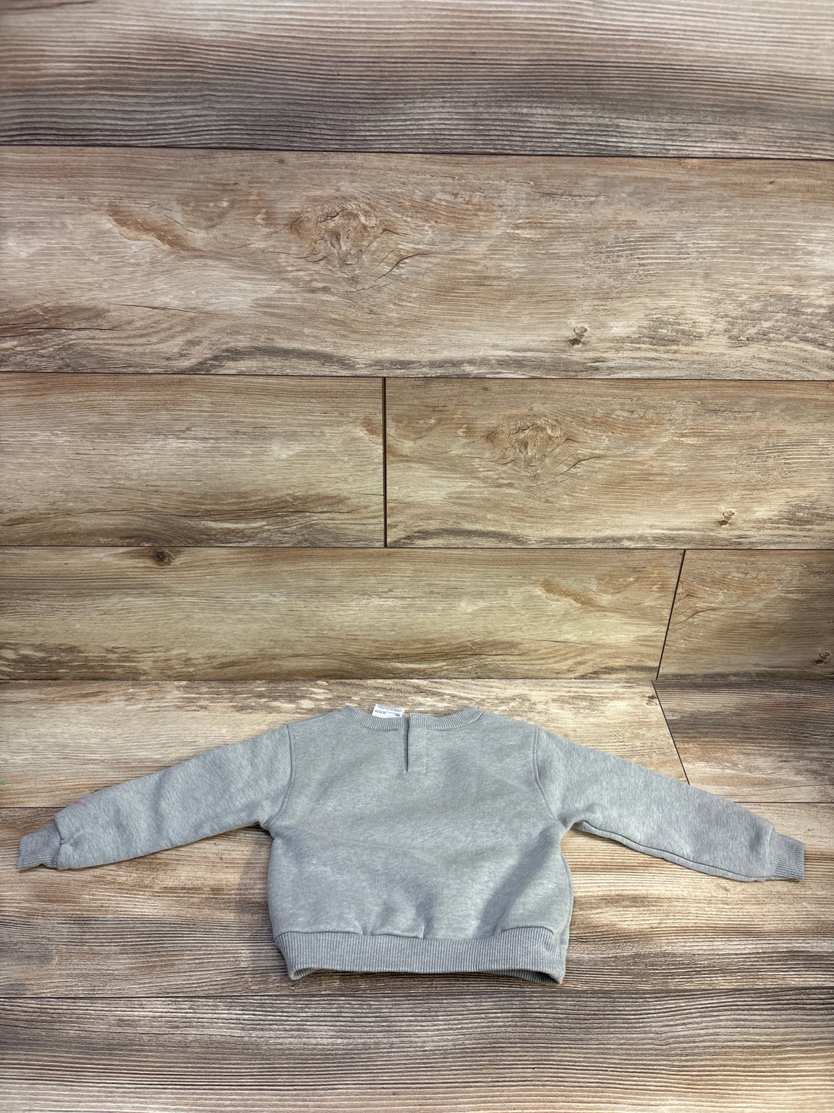Back view of grey Nike toddler pullover sweatshirt with ribbed cuffs and hem and back keyhole on wood background
