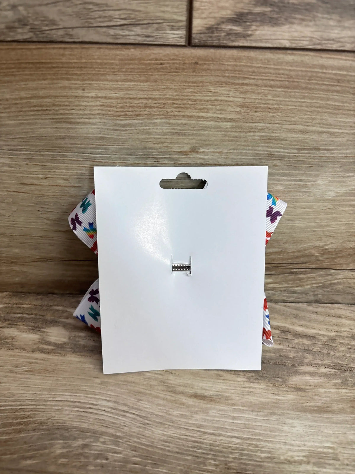 Front view of large bow with butterfly print on white ribbon, pinned to white card on wood background