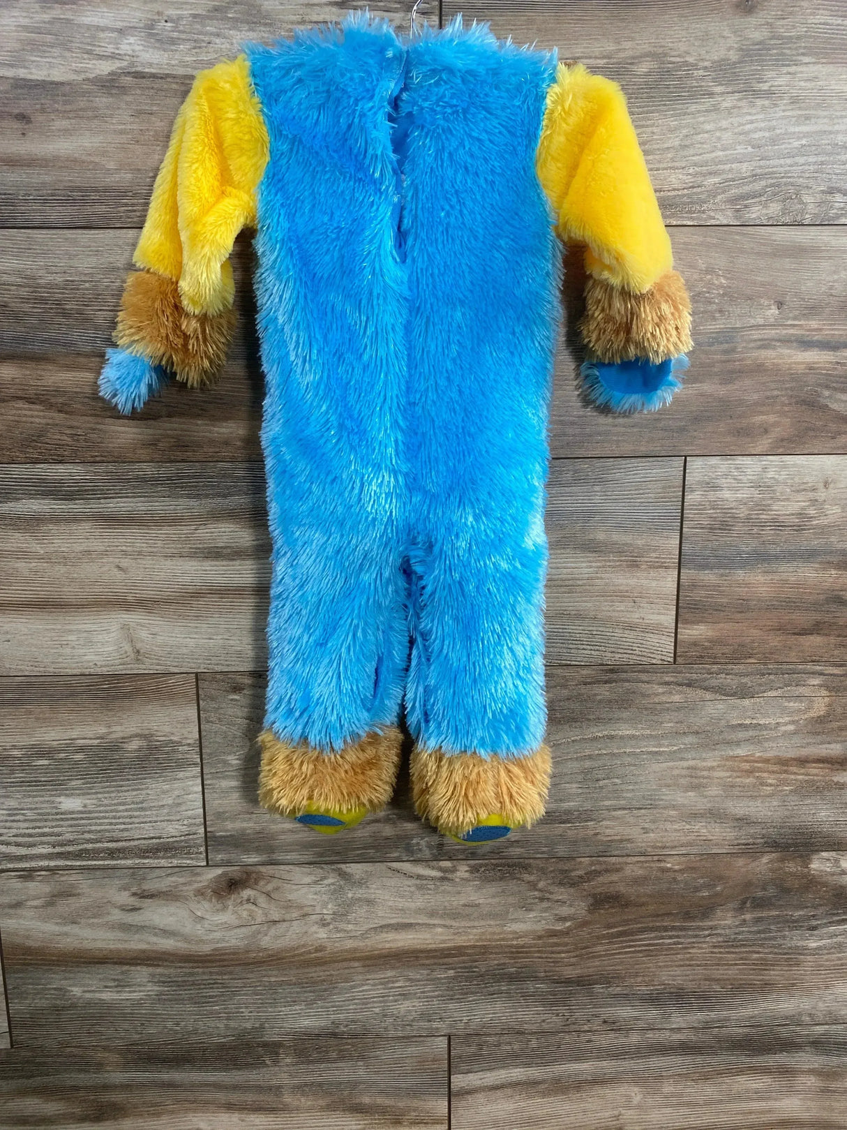 Back view of 6-12 mo plush monster costume showing blue fuzzy body, yellow sleeves, brown cuffed wrists and attached feet on wood floor
