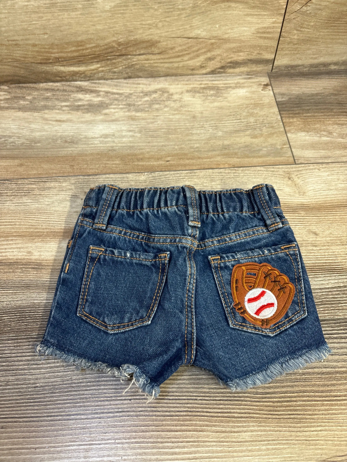 Back view of Old Navy blue denim shorts with elastic waistband, frayed hem, and baseball glove patch on right pocket