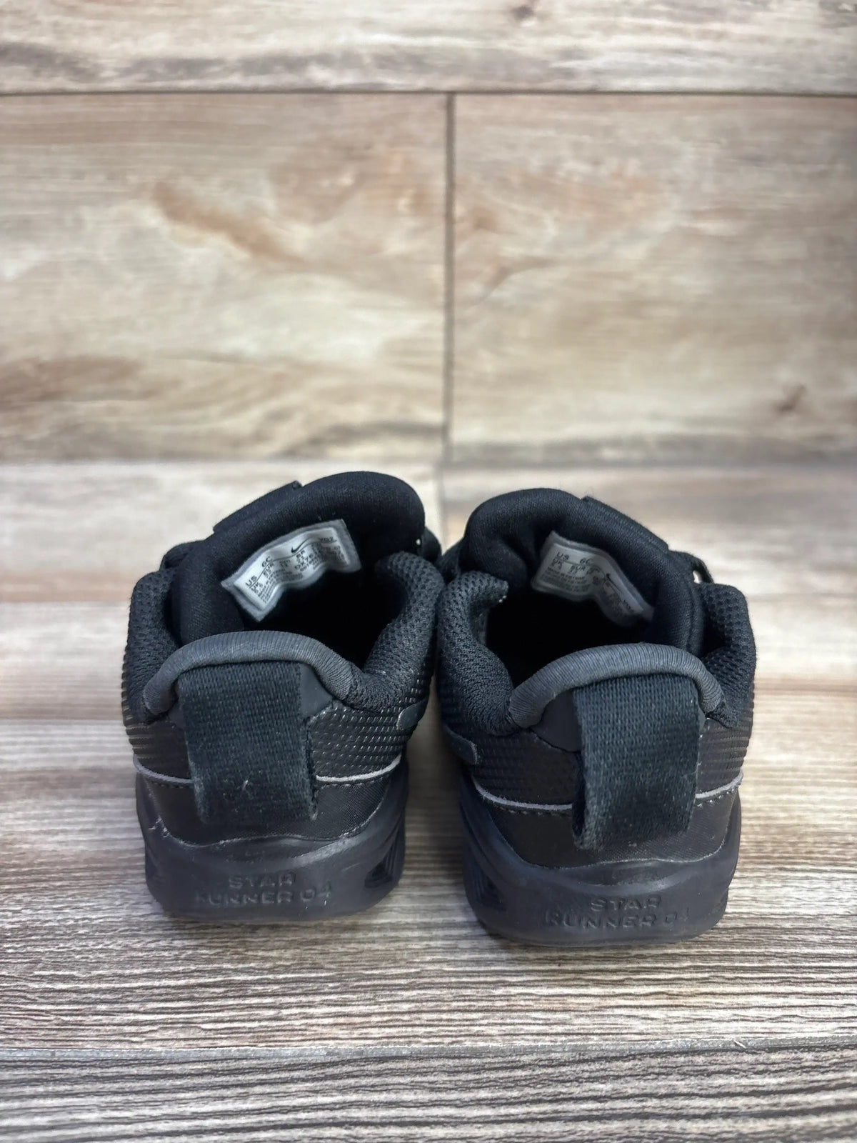 Rear view of toddler Nike Star Runner 4 TD triple black sneakers showcasing heel pull tabs and padded collars on wood floor background