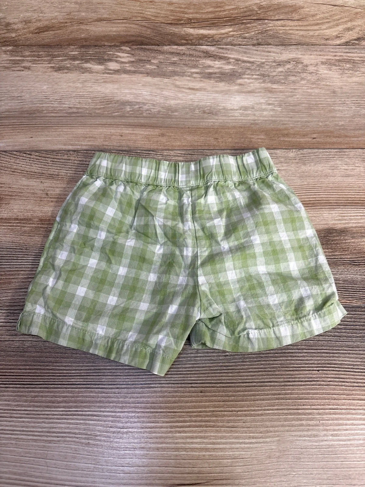 Flat lay of green gingham baby shorts showing elastic waistband and cuffed hems on wooden background