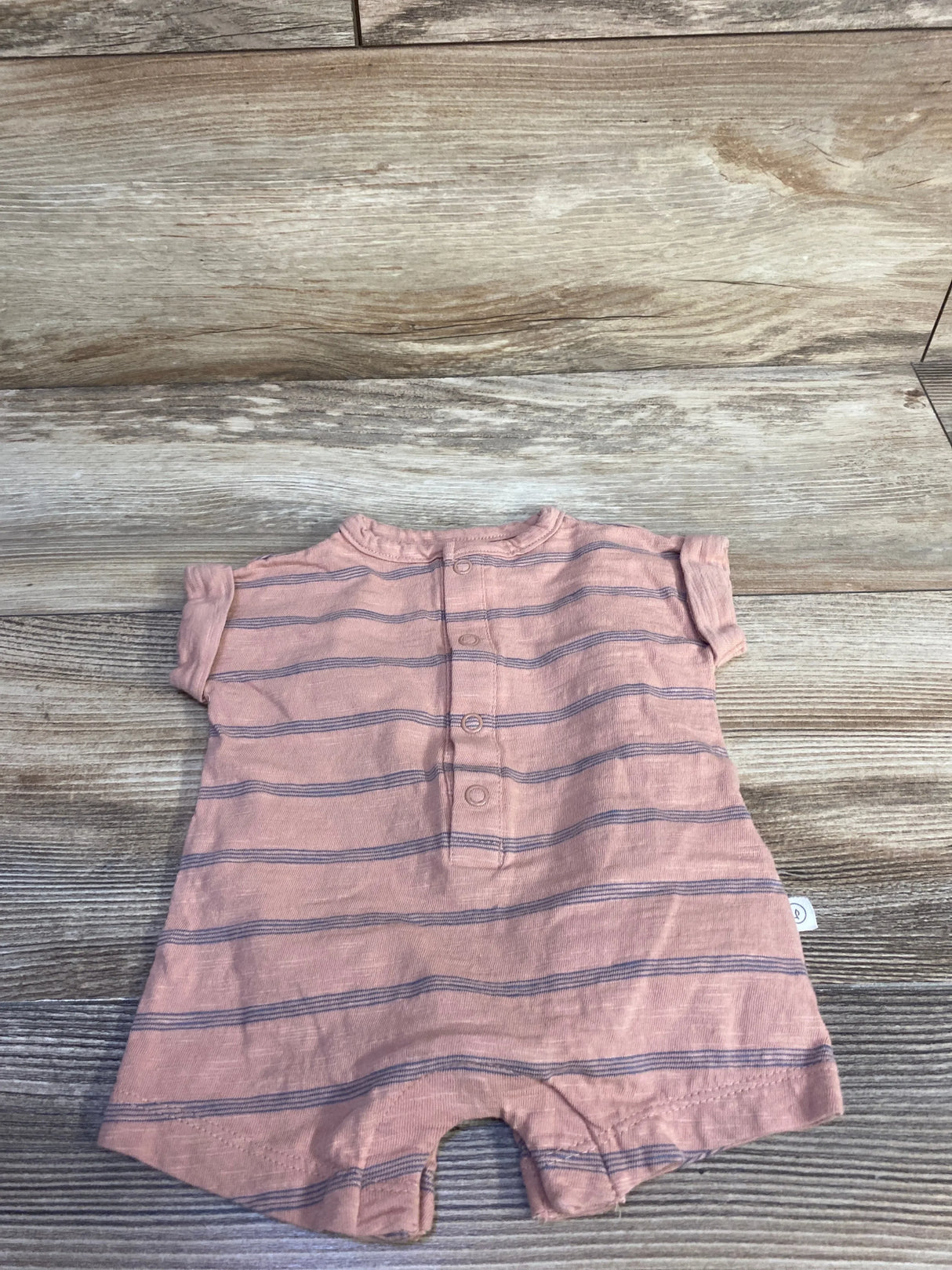 Flat lay of newborn Little Planet Organic shortie romper in muted orange with navy horizontal stripes and front snap placket on wood background