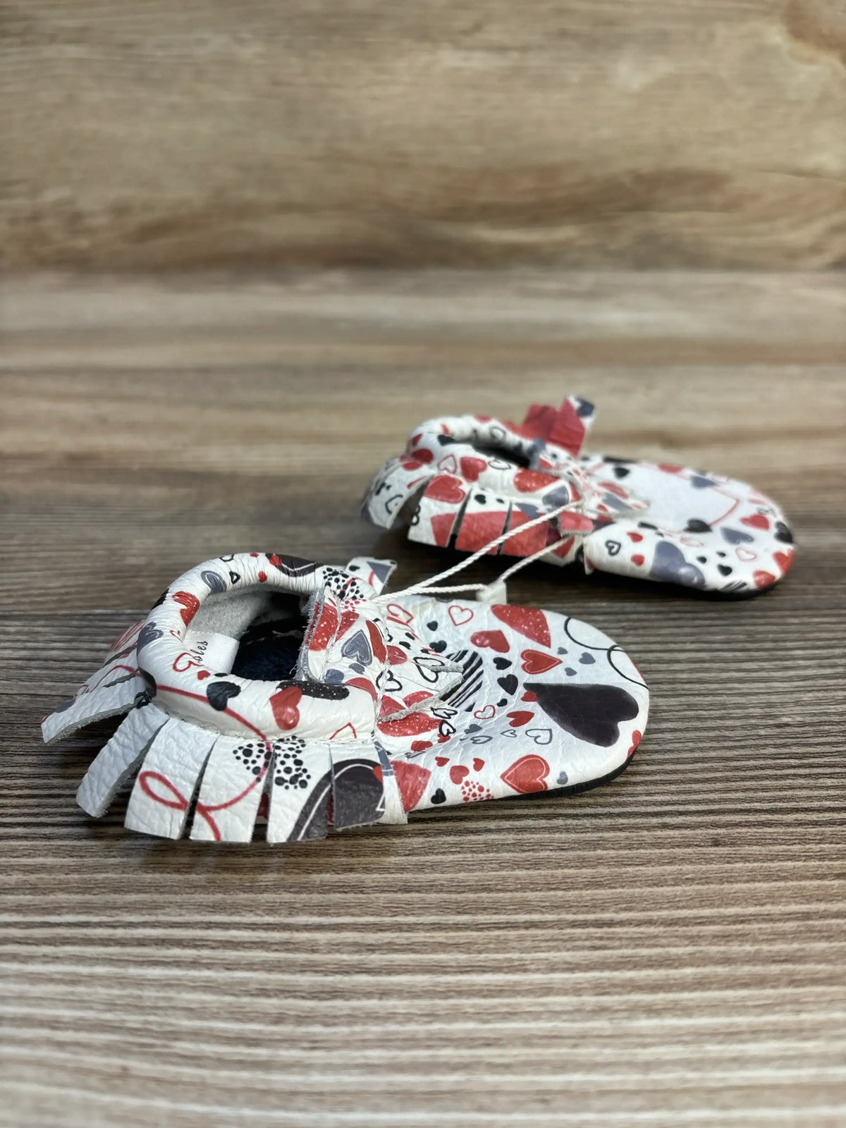 Heart print baby moccasins with soft leather and fringe on wooden background