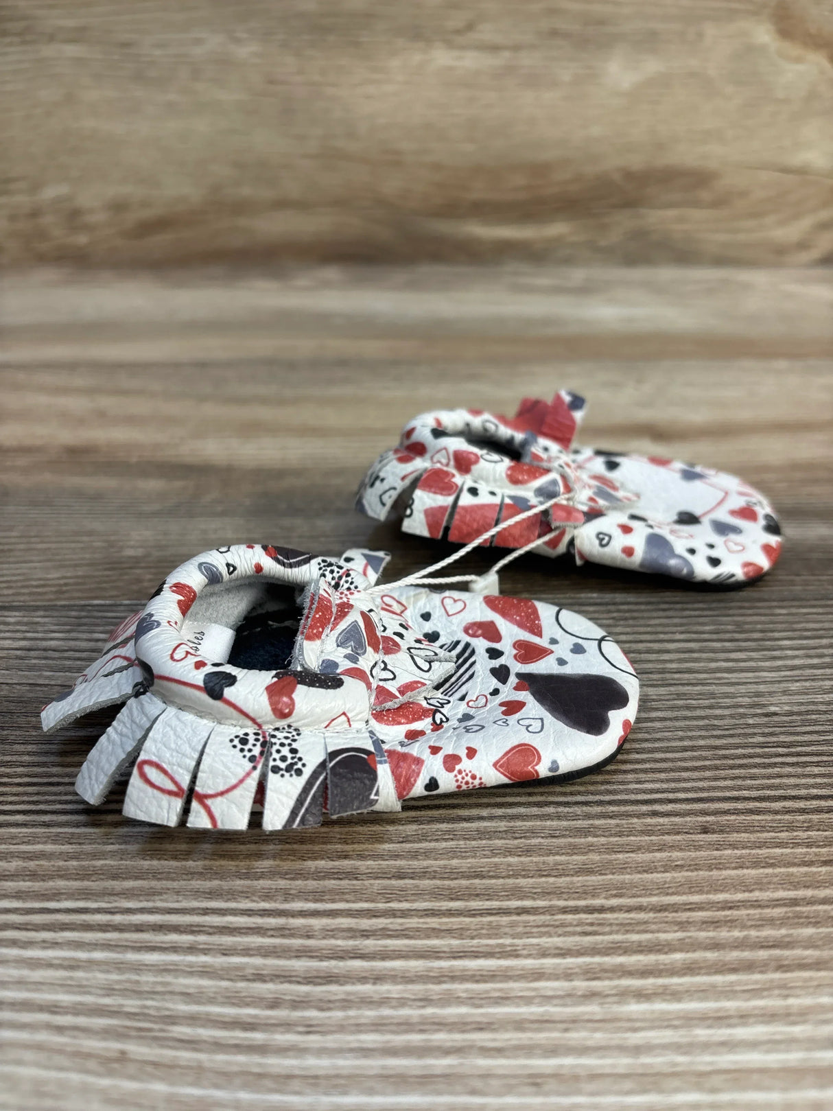 Heart print baby moccasins with soft leather and fringe on wooden background