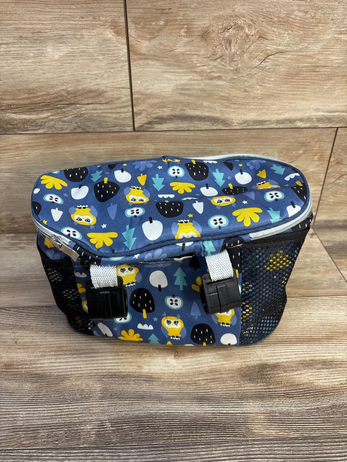 Blue baby gear bag with yellow owl and tree patterns on a wooden surface
