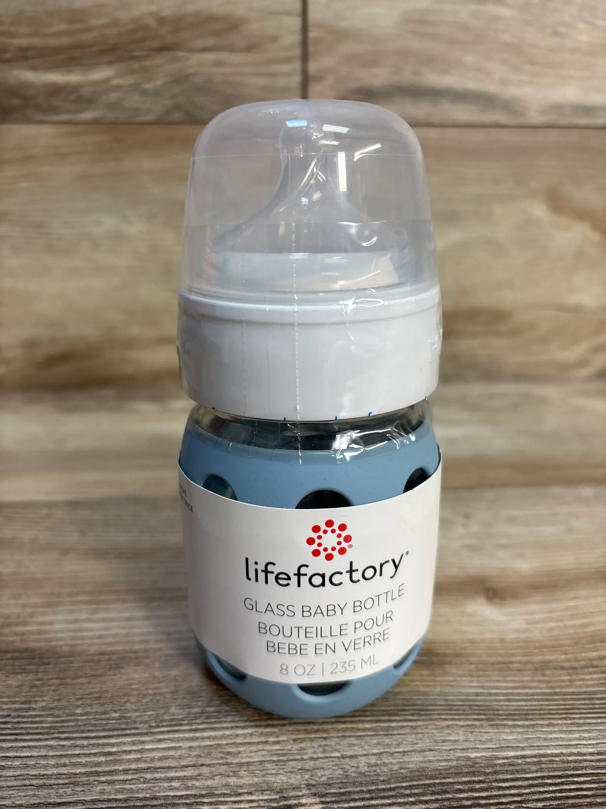 Front view of LifeFactory glass baby bottle showcasing blue silicone sleeve, clear cap, and 8 oz label on wood background