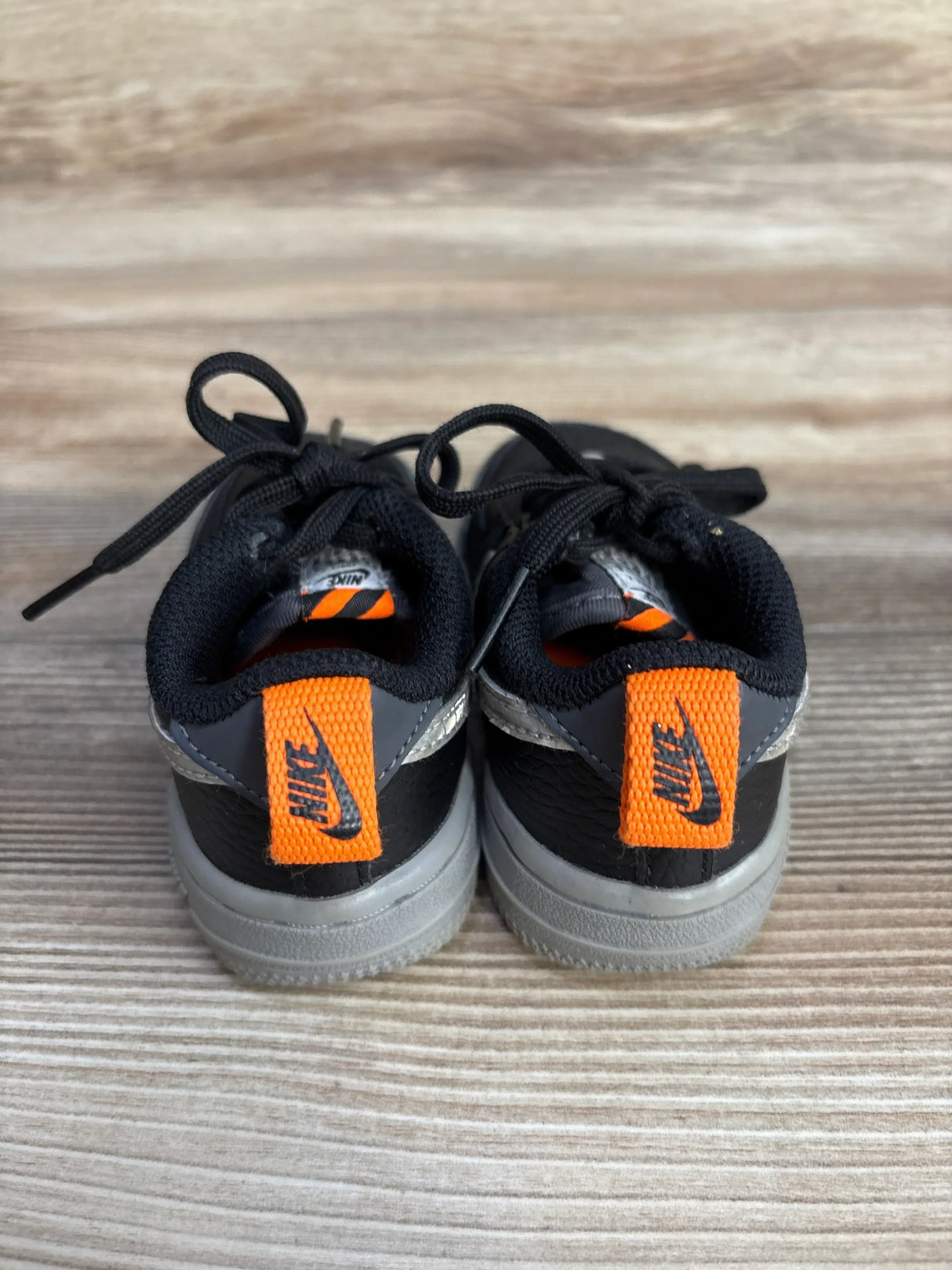 Back view of black and gray Nike toddler sneakers with bright orange Nike tags on wooden floor