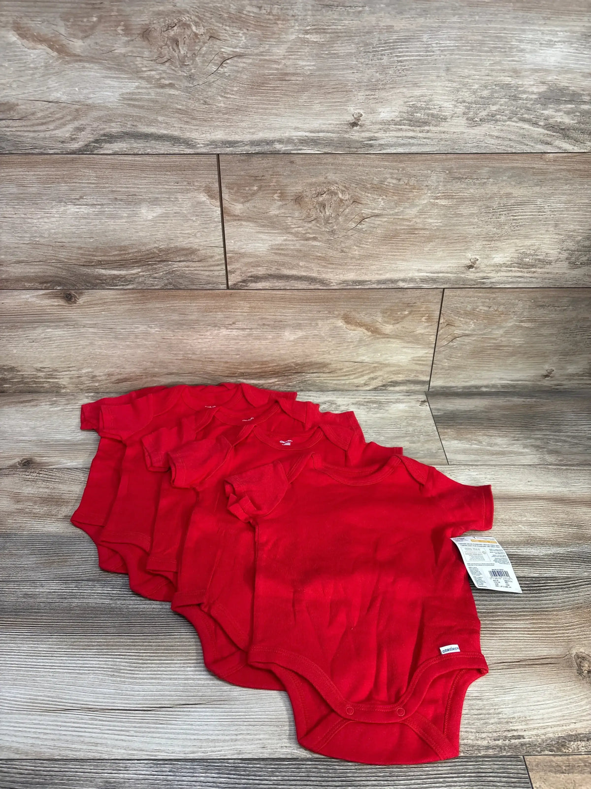 Front view of five red Gerber bodysuits size 3-6 months showing snaps and tag on wood background