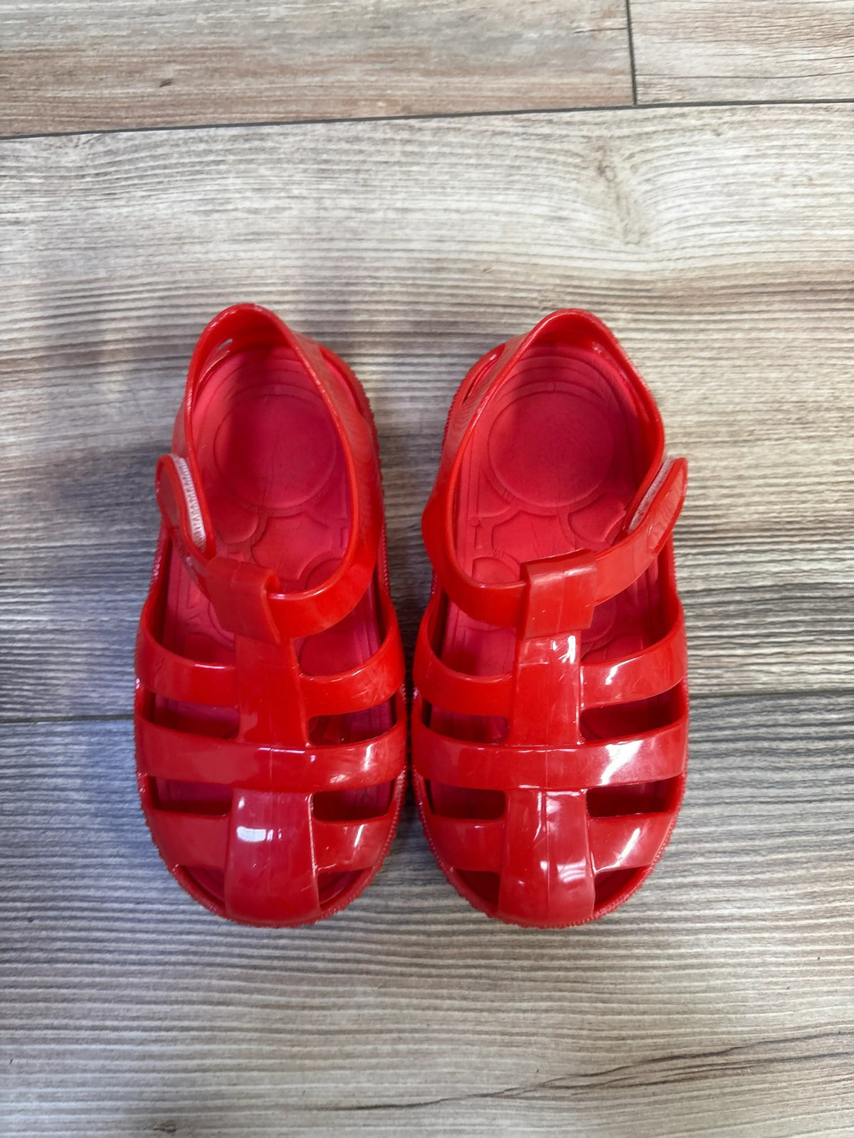 Top view of red Jelly Fisherman Sandals showcasing strappy fisherman design and hook and loop closures on a wood-grain background