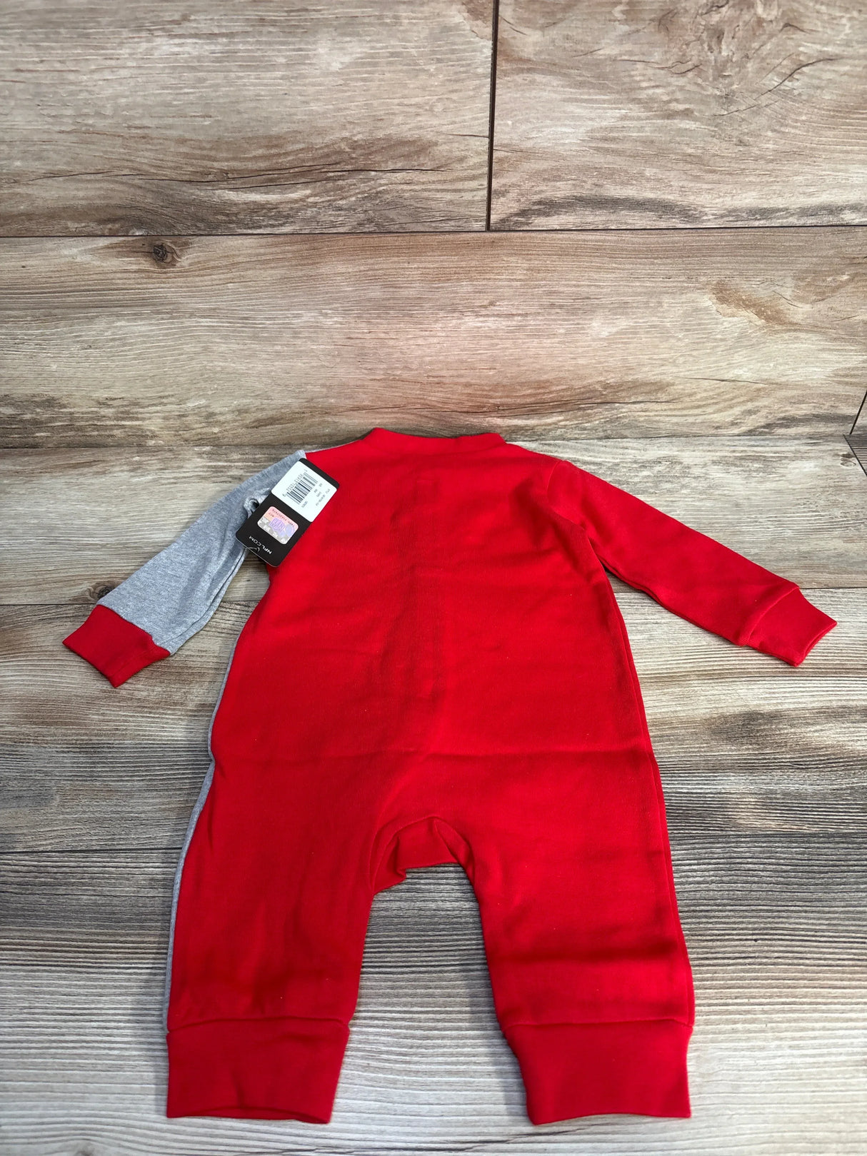 Red baby romper with one gray sleeve on wood background, clothing tag attached