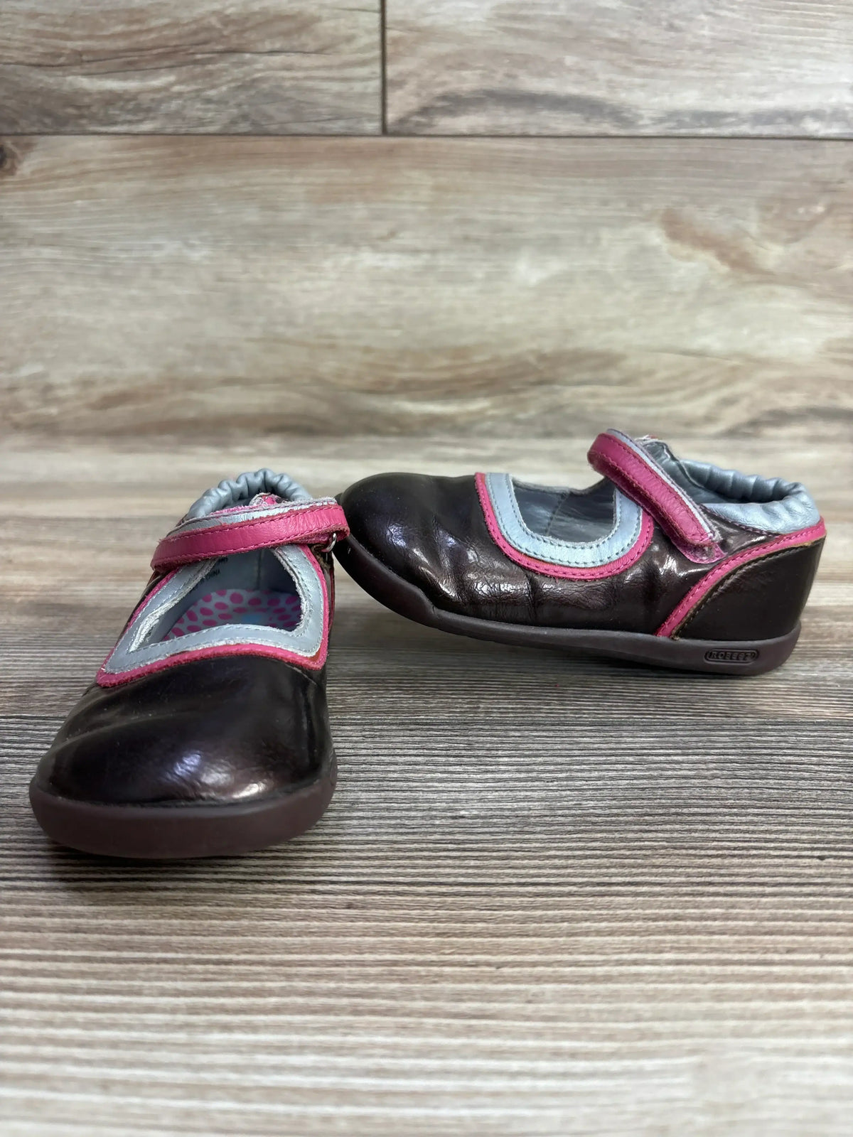Pair of brown leather toddler shoes with pink and gray trim on wooden surface