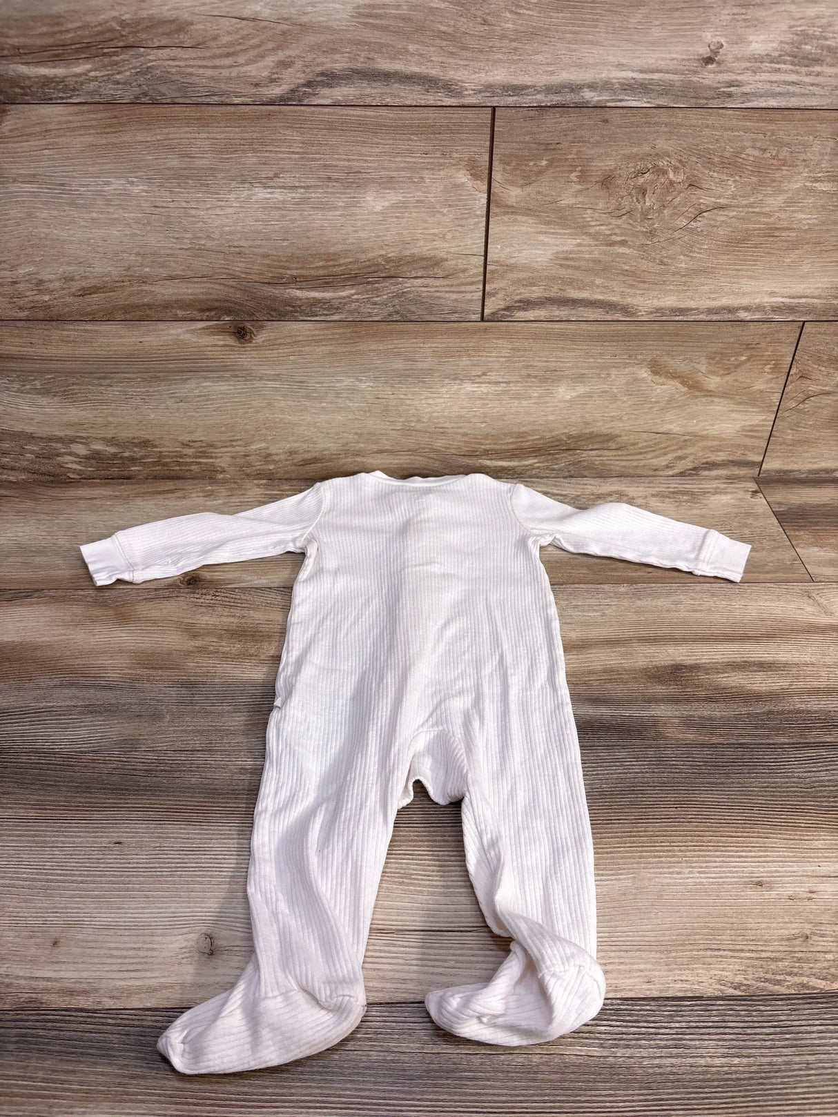 Flat lay of white ribbed footed sleeper, 9 months, showing ribbed texture and built-in feet on light wood floor