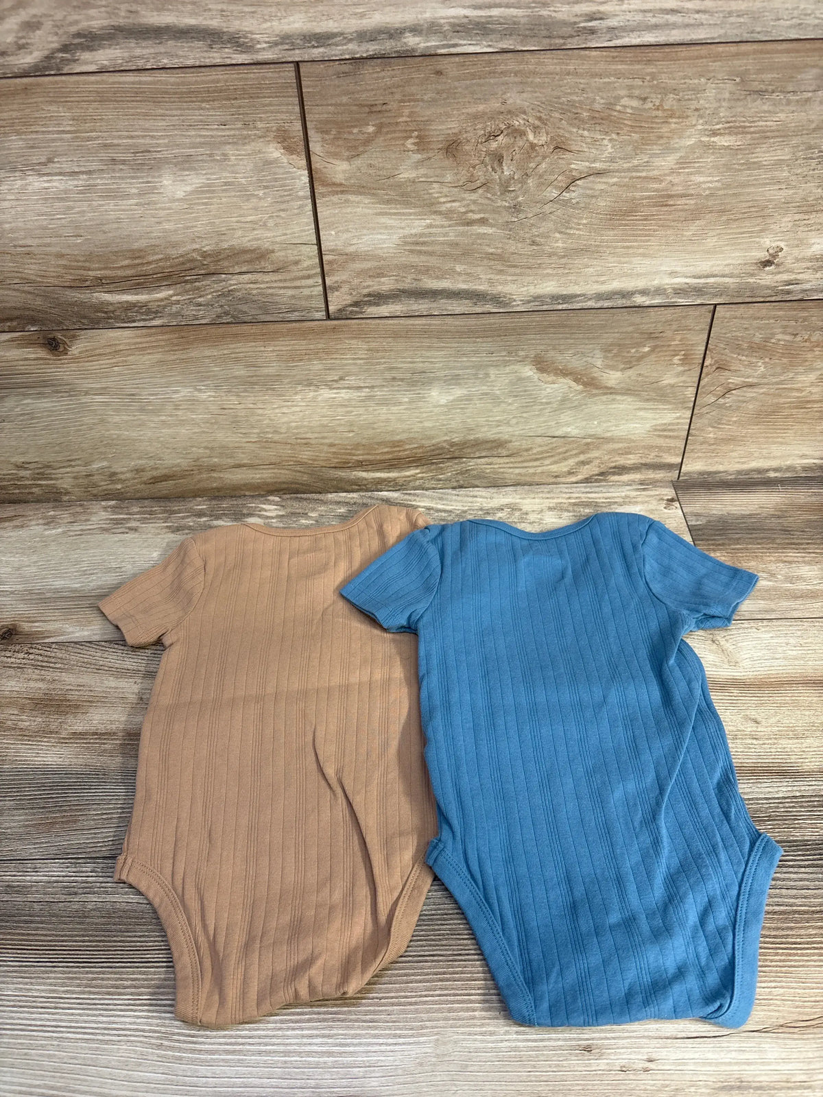 Front view of Cloud Island 2pk ribbed bodysuit set showcasing vertical ribbing and short sleeves on a wood grain background